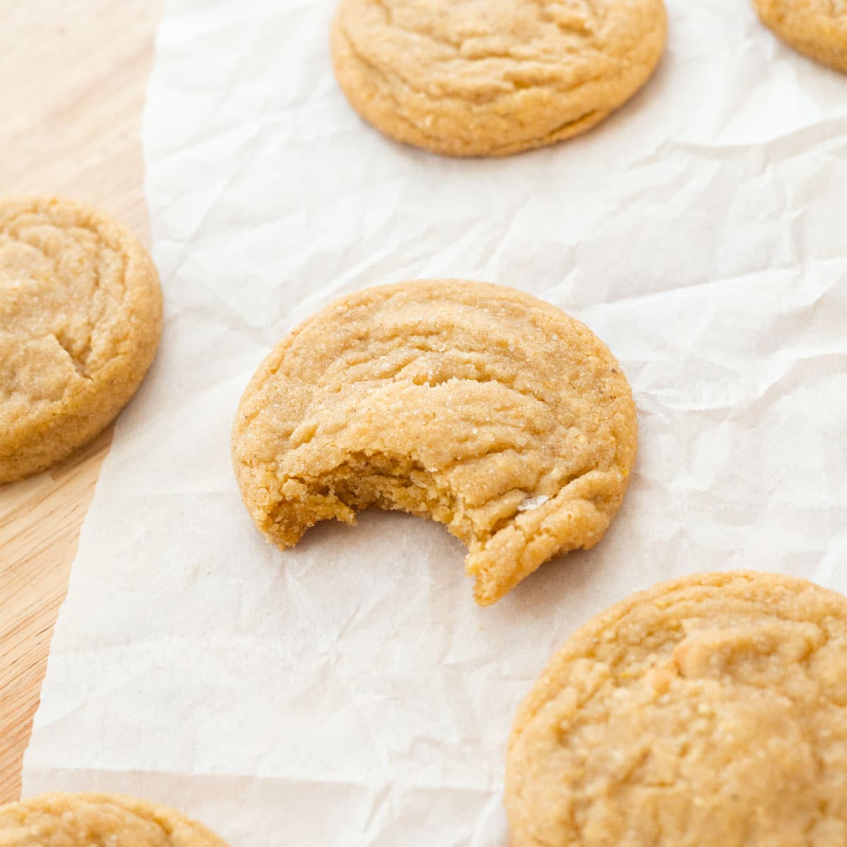 Corn sugar cookies spread across parchment paper, with a single bite taken from the center cookie.