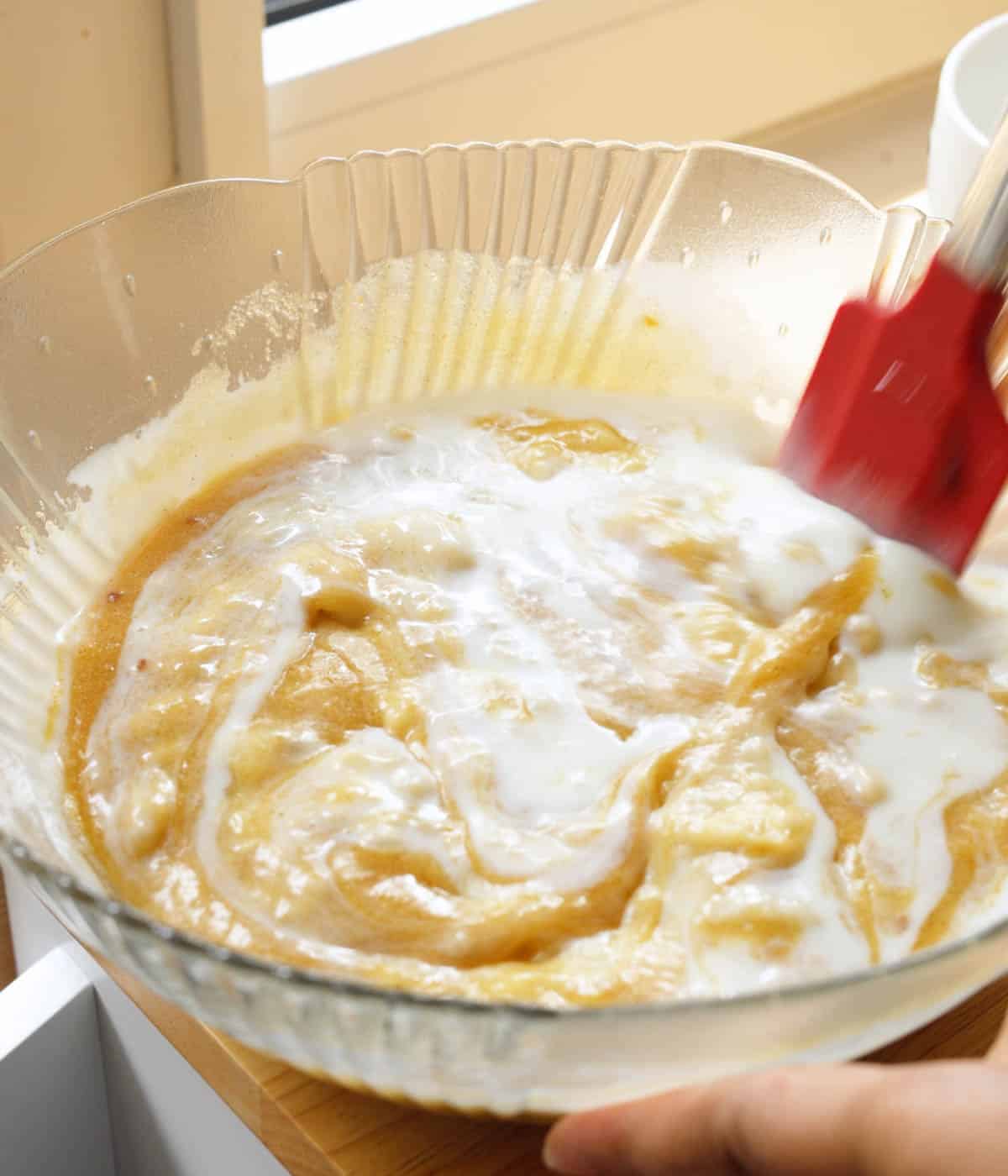 Wet mixture of butter, sugar, eggs, vanilla, buttermilk, and mashed bananas mixed together in a glass bowl.
