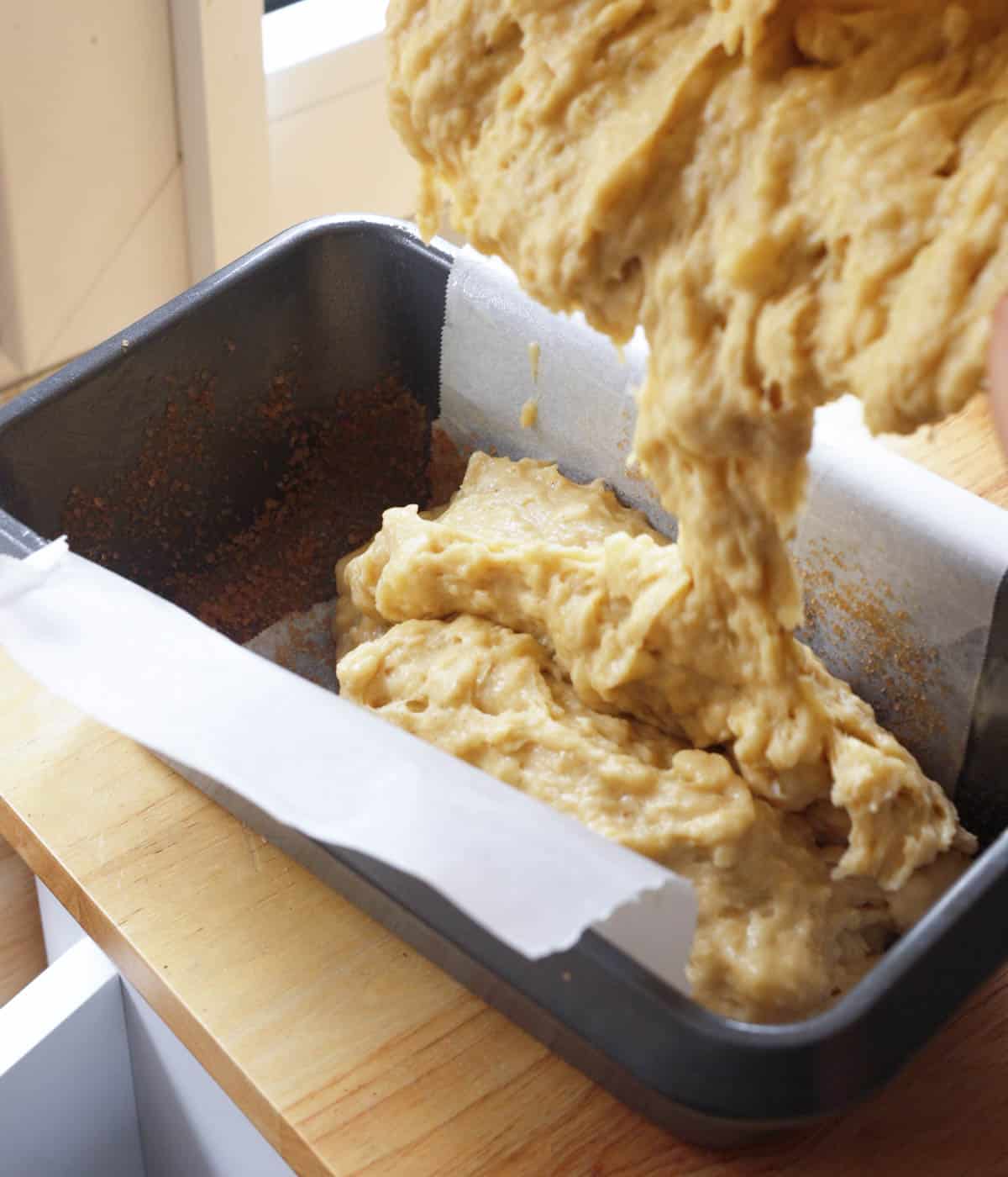 Pouring banana bread batter into loaf pan.
