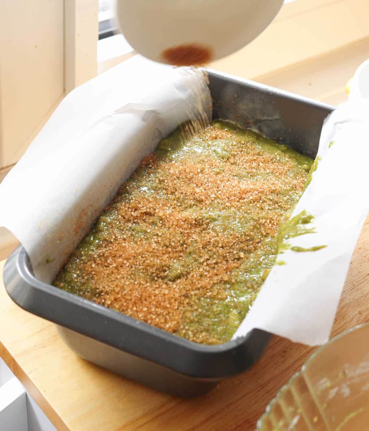 Matcha banana bread batter in loaf pan with turbinado sugar sprinkled on top.