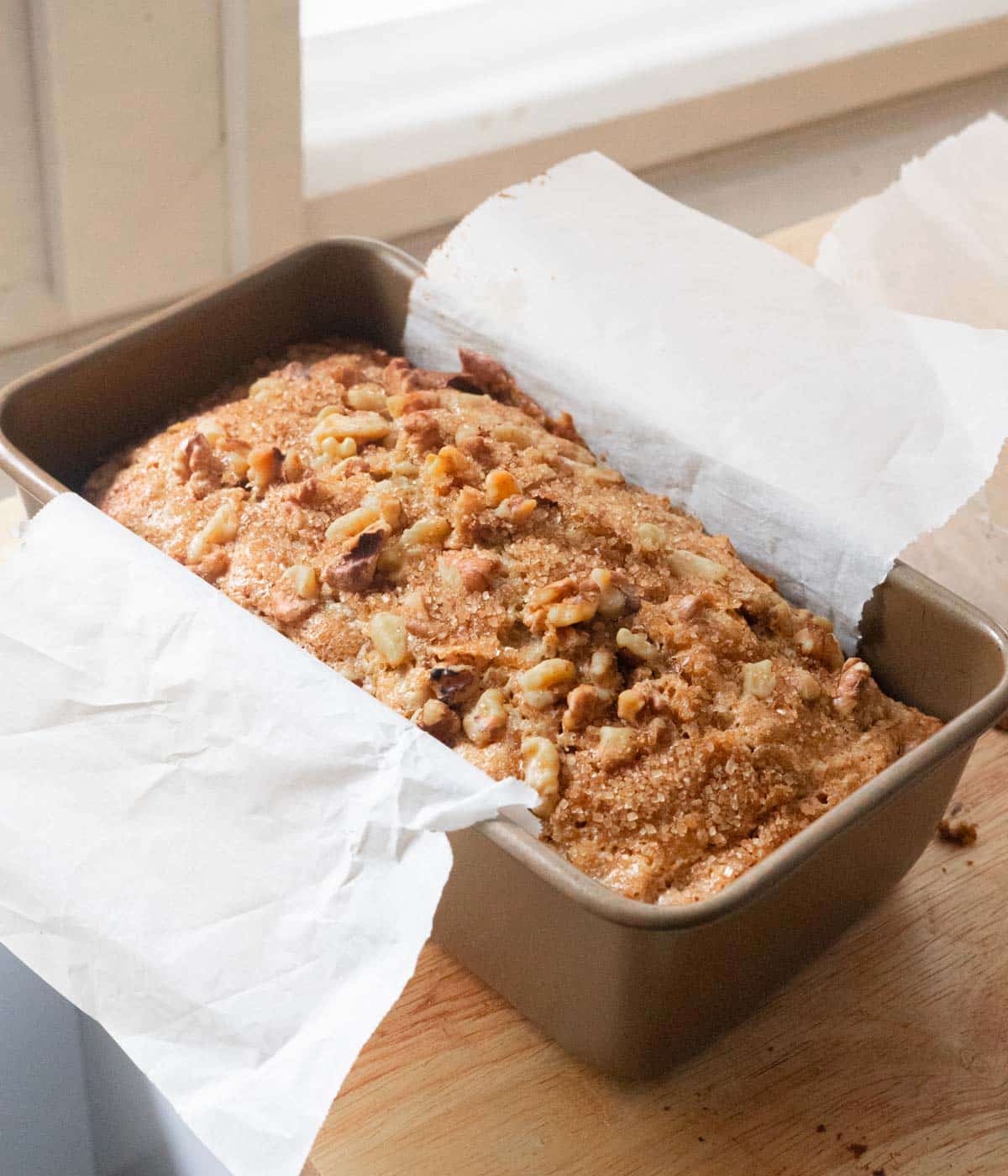 Walnut banana bread in loaf pan, topped with turbinado sugar and walnuts.