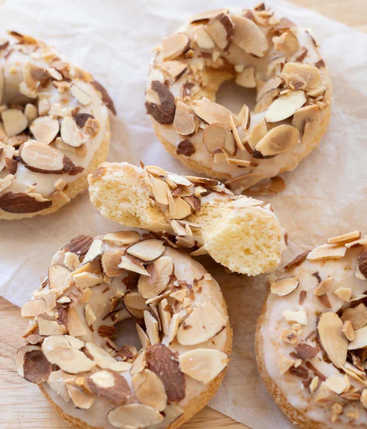 Almond mochi donuts on wooden table lined with parchment paper; cross-section shows chewy texture.