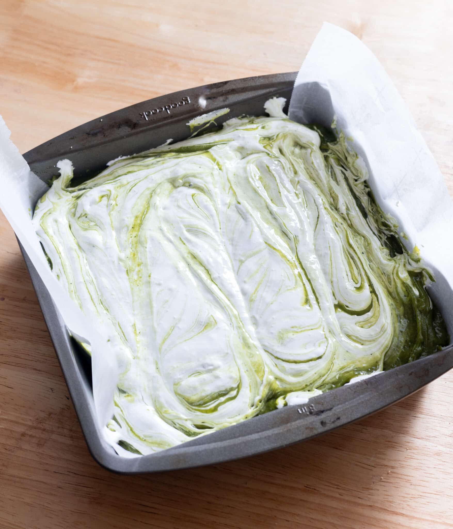 Matcha brownie batter topped with marshmallow fluff; batter is slightly stirred in to create a marbling effect.