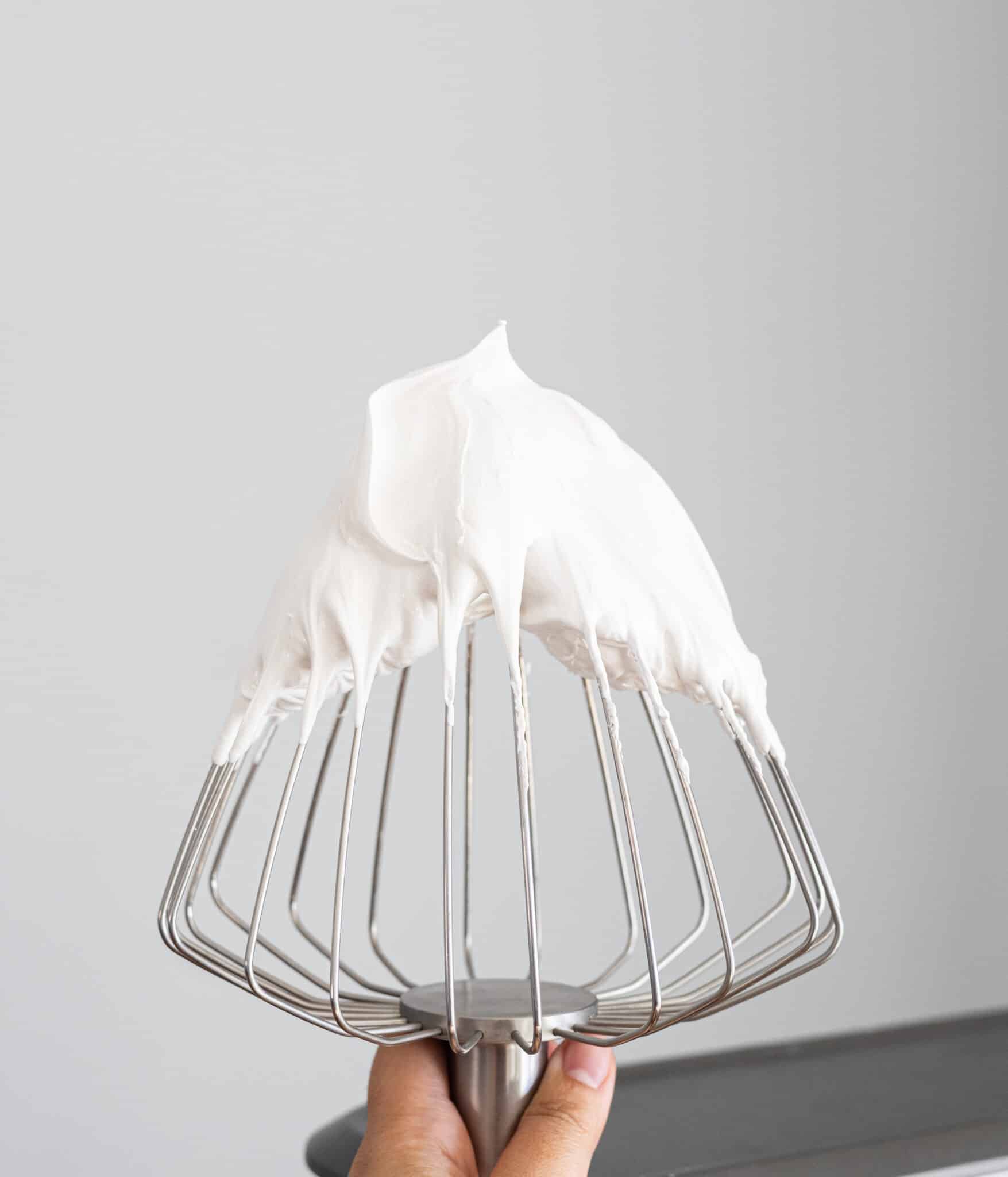 Fluffy Swiss meringue with stiff peaks on a balloon whisk.