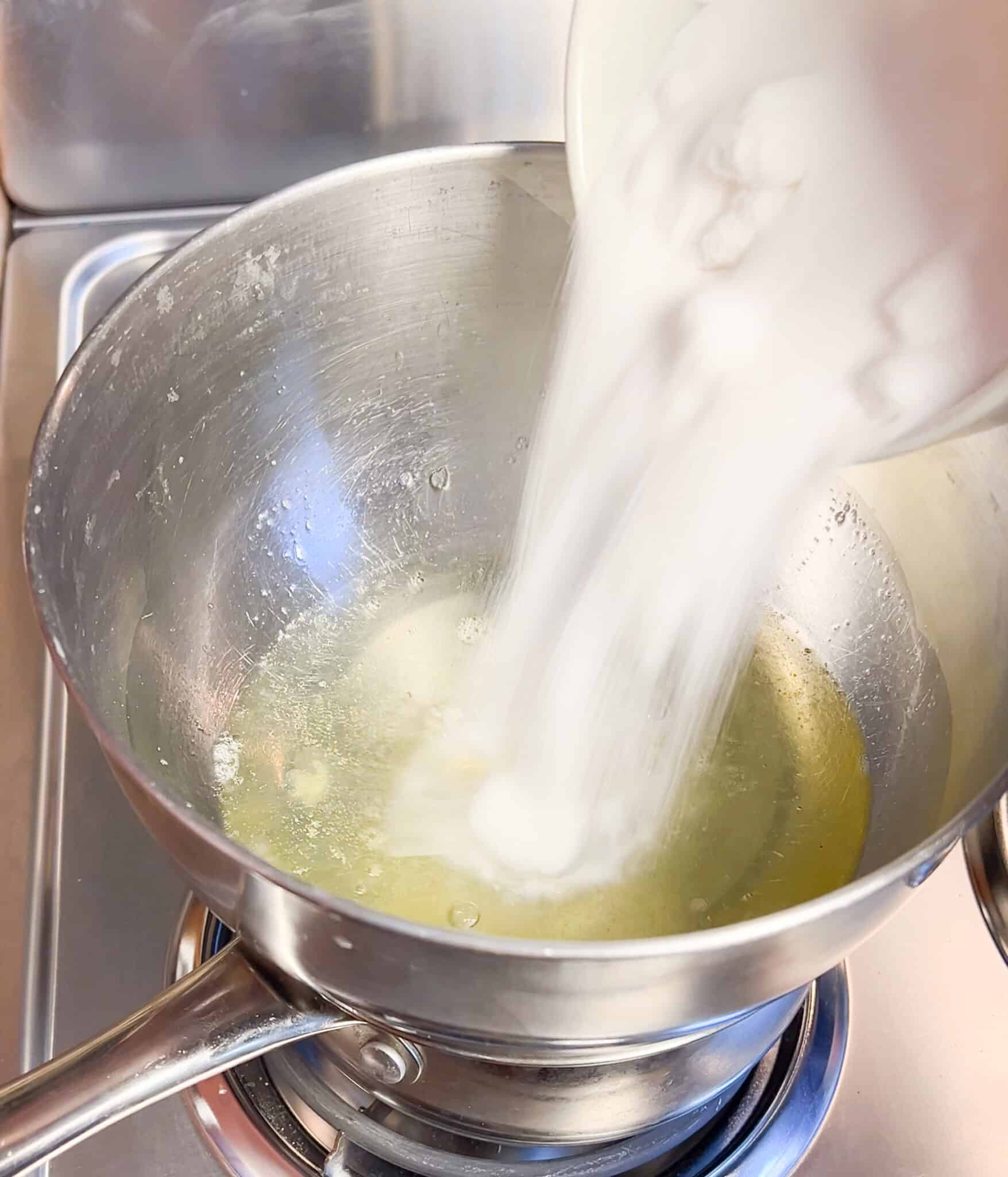 Adding sugar to a bowl of egg whites over a double boiler.