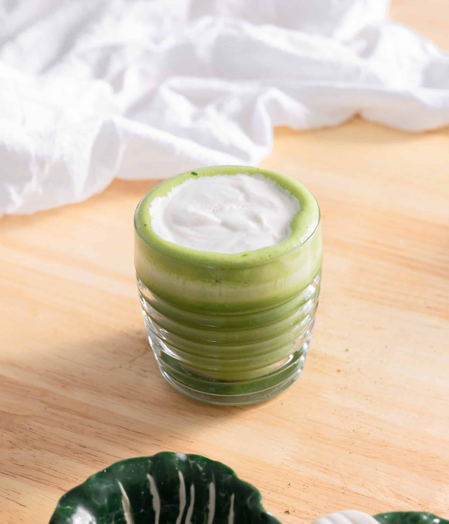 Brown sugar cold foam on top of a matcha latte in a glass cup.