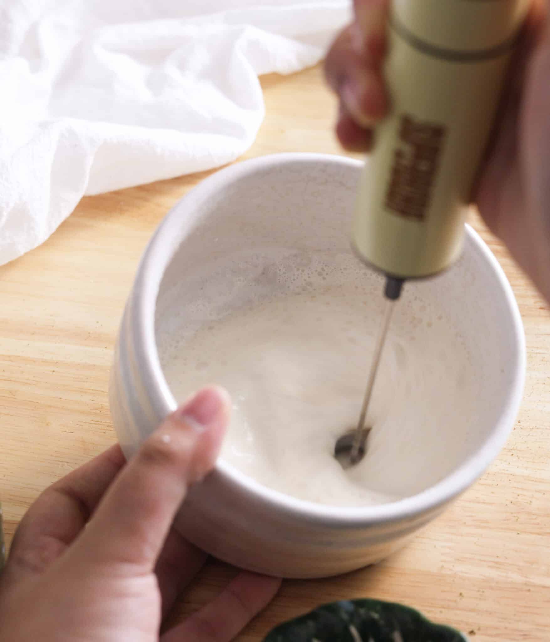 Using a frother to mix brown sugar cold foam ingredients in a small bowl.