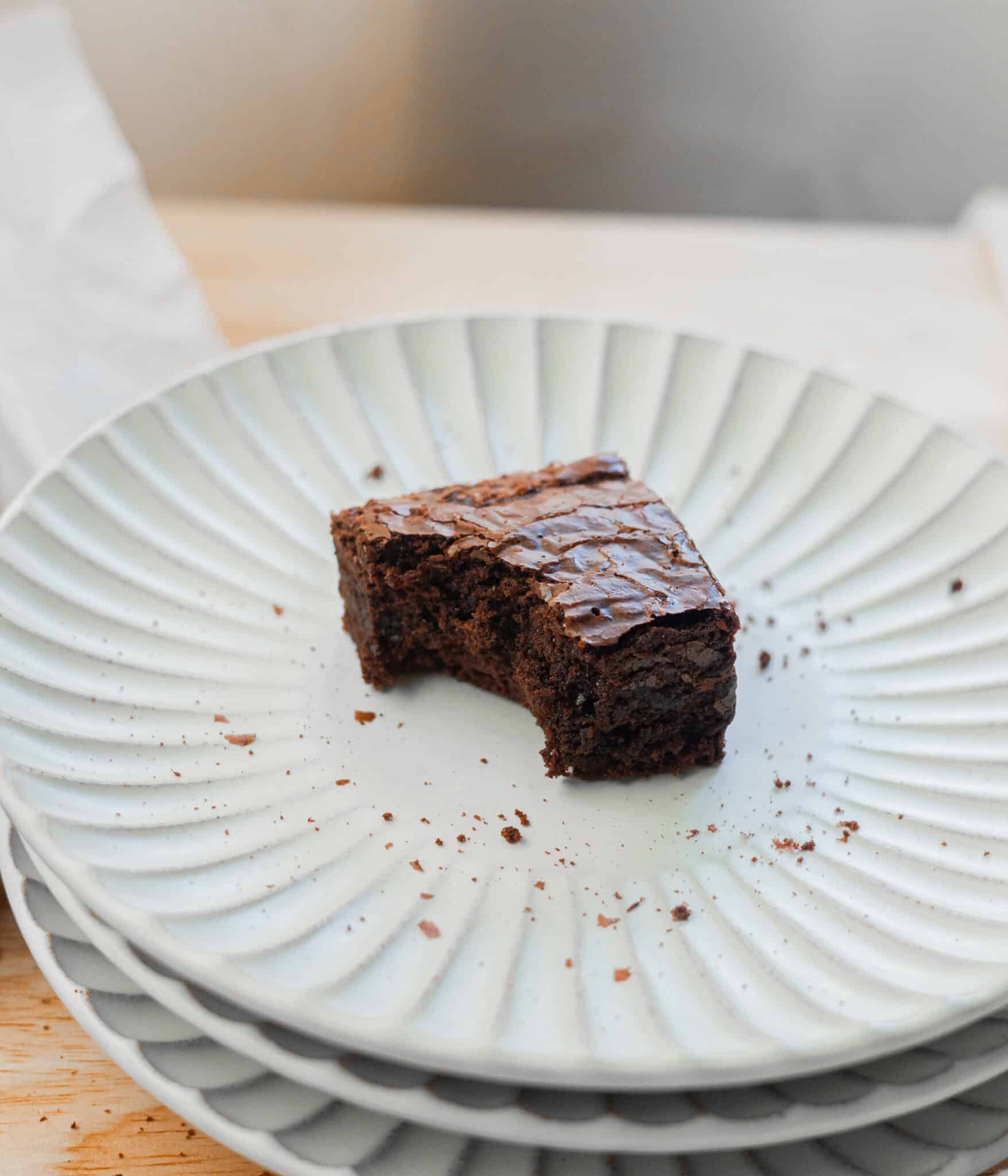 Shiny, crinkly top brownie with a bite taken out of it on top of a plate.