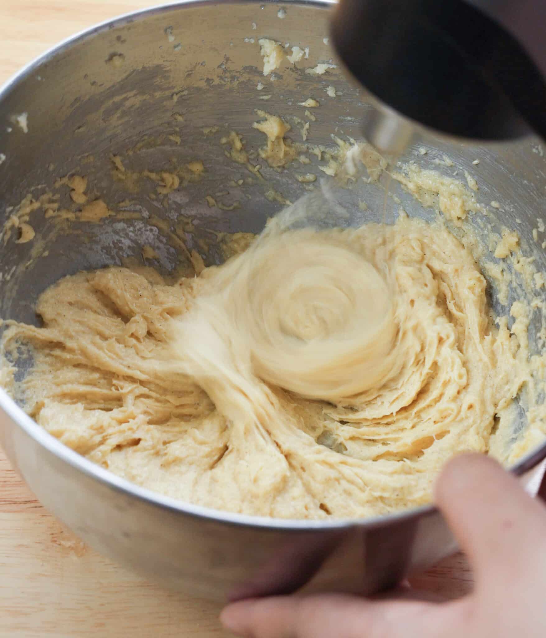 Using a whisk to mix wet ingredients in a stainless steel bowl.