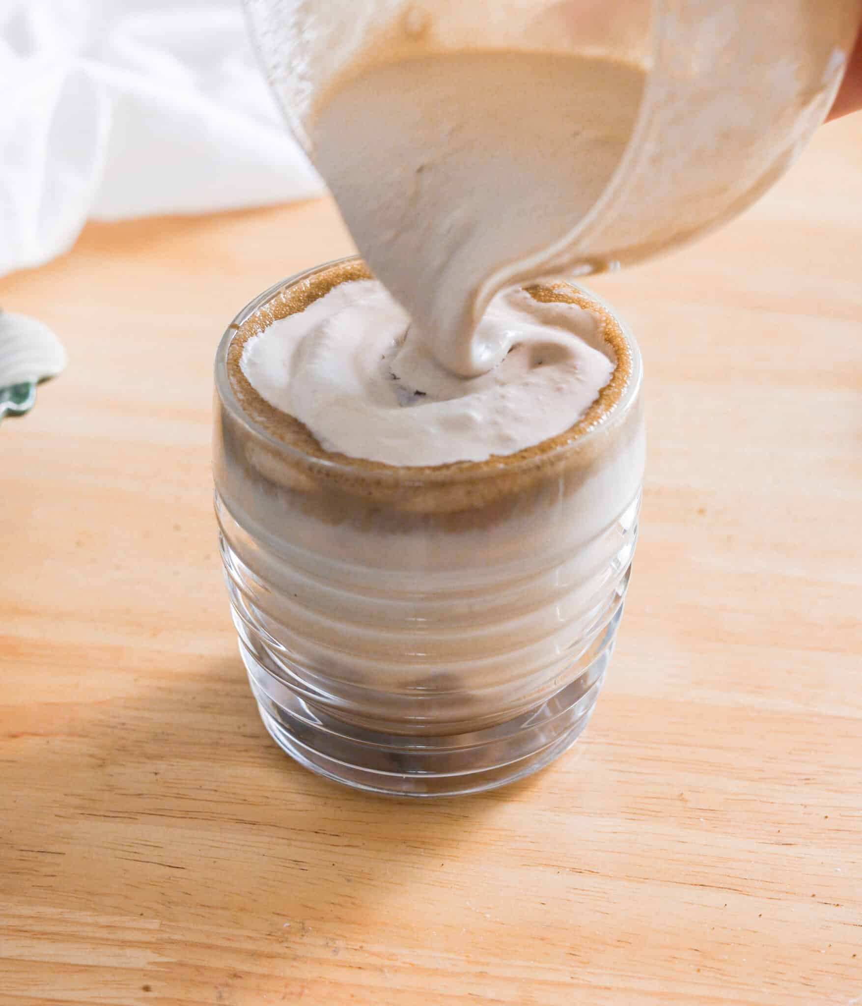 Pouring hojicha cold foam over hojicha latte.