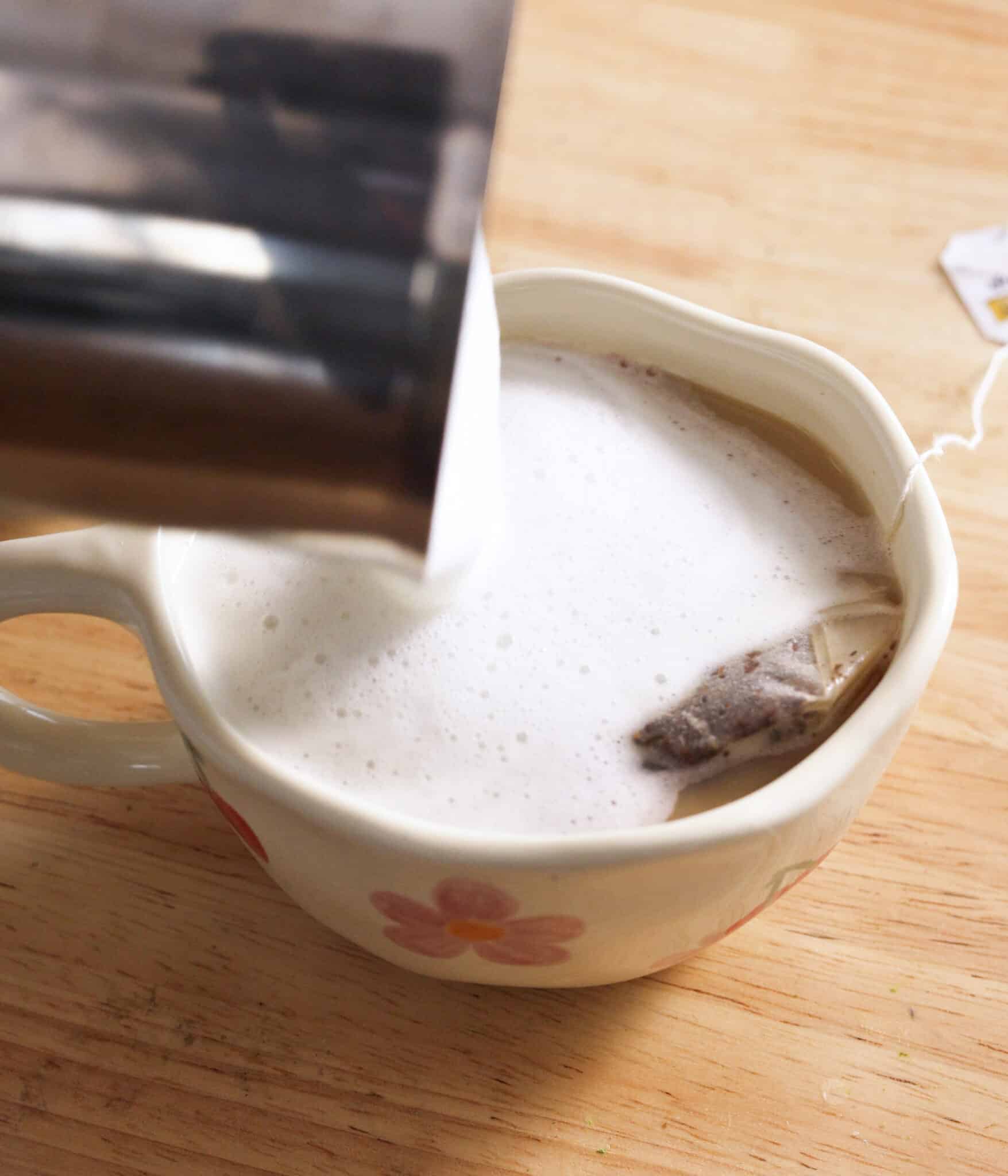 Pouring steamed milk over earl grey tea to make a london fog.
