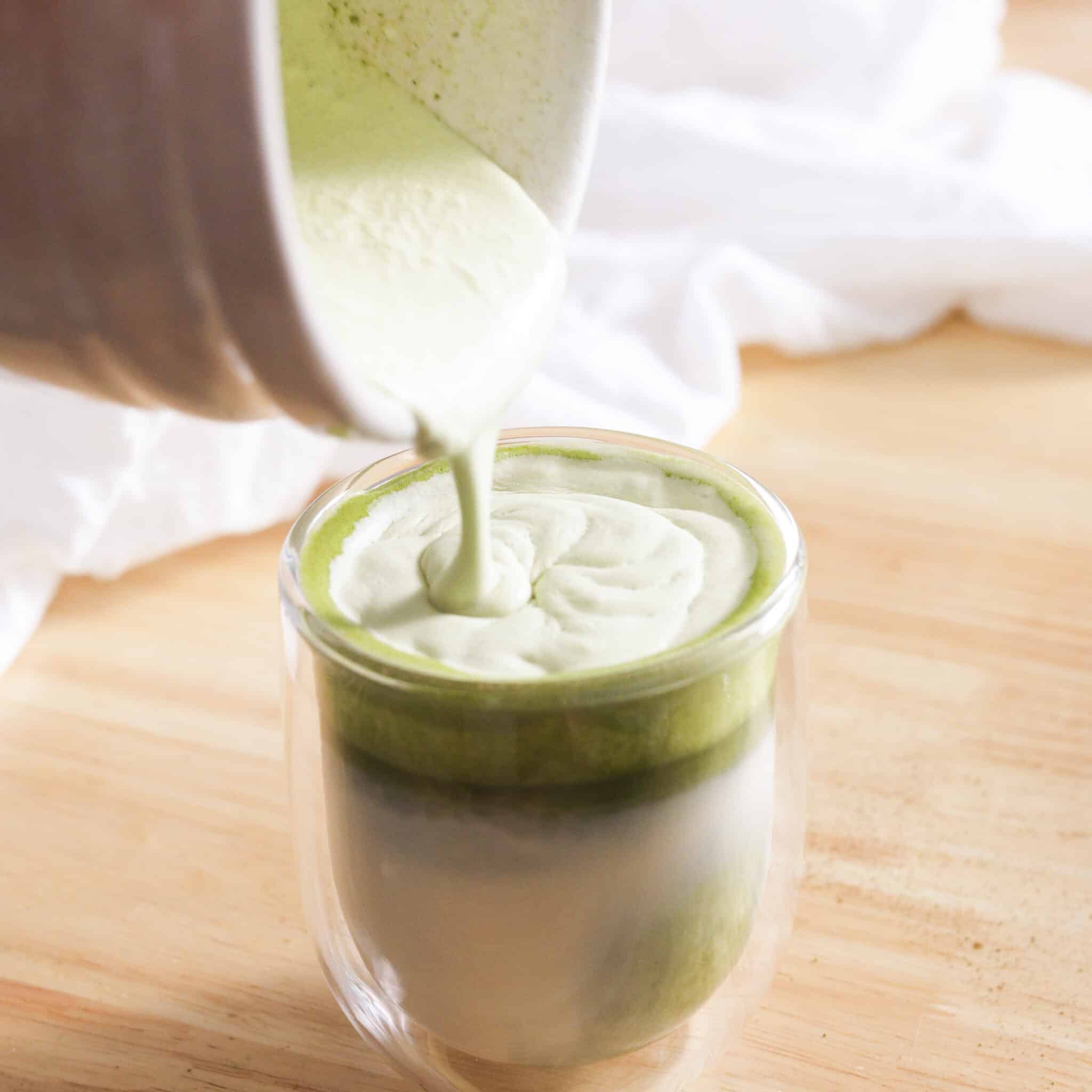 Pouring matcha cold foam on top of matcha latte.