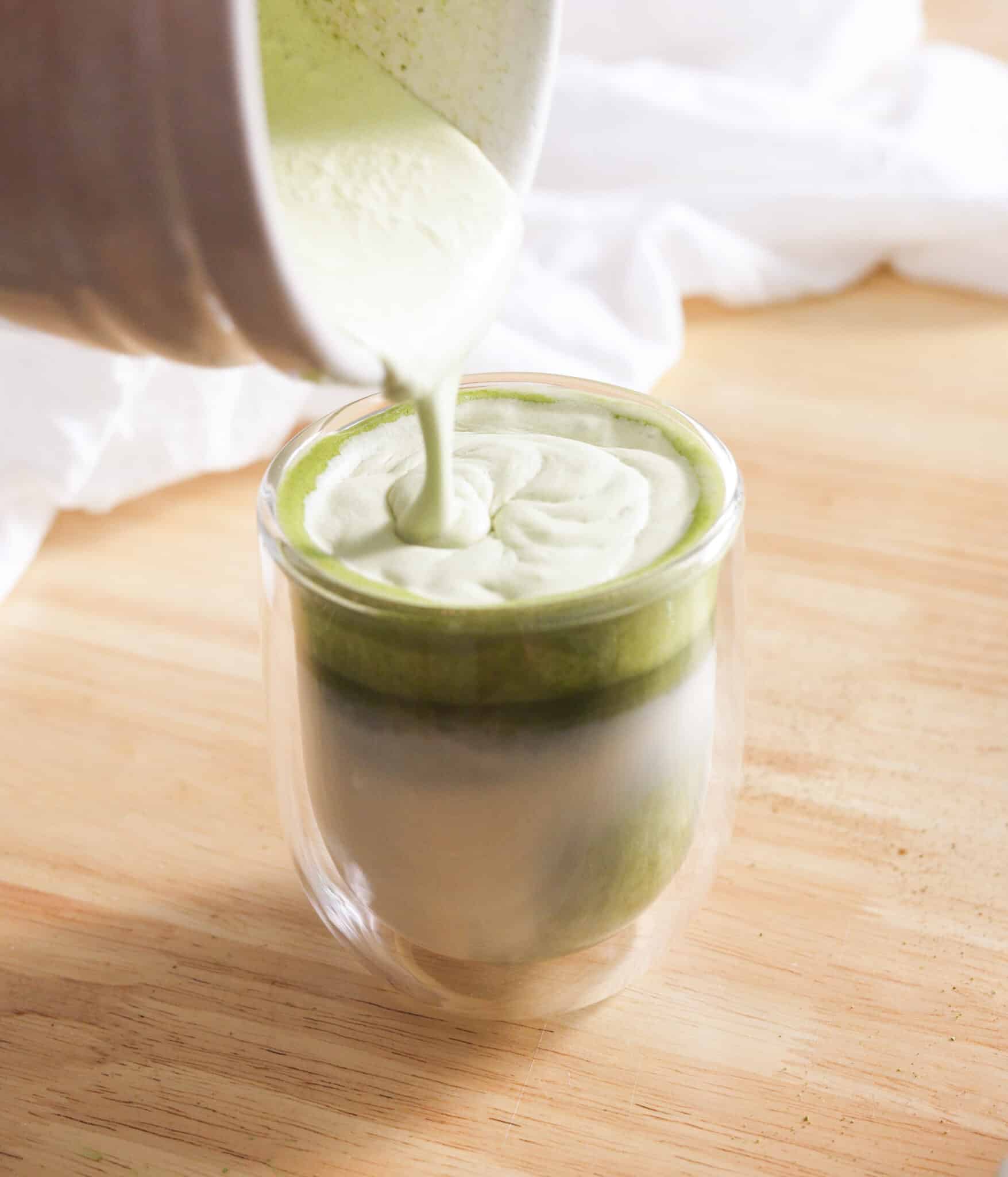 Pouring matcha cold foam on top of matcha latte.