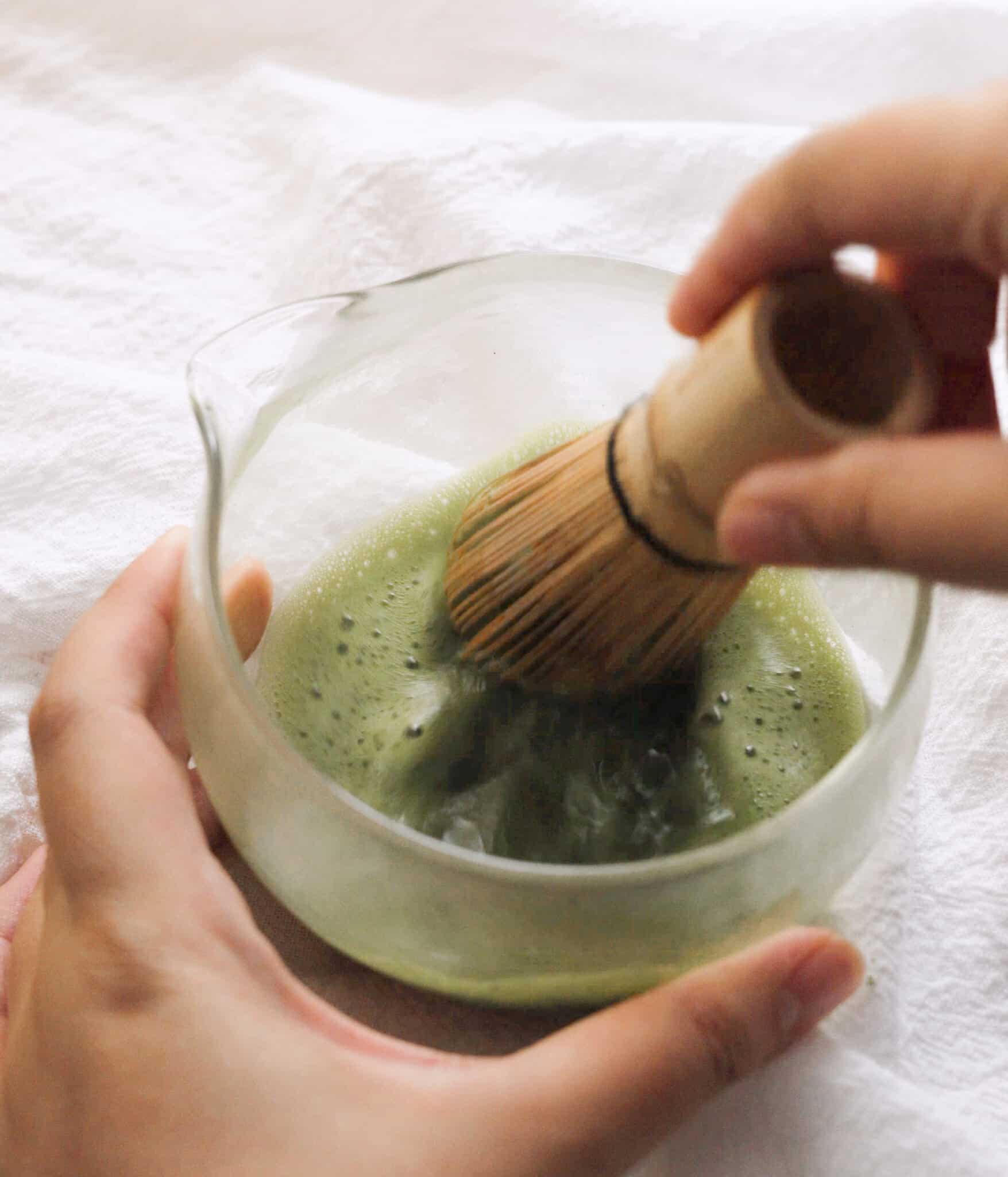 Whisking matcha and hot water in a bowl using a chasen.