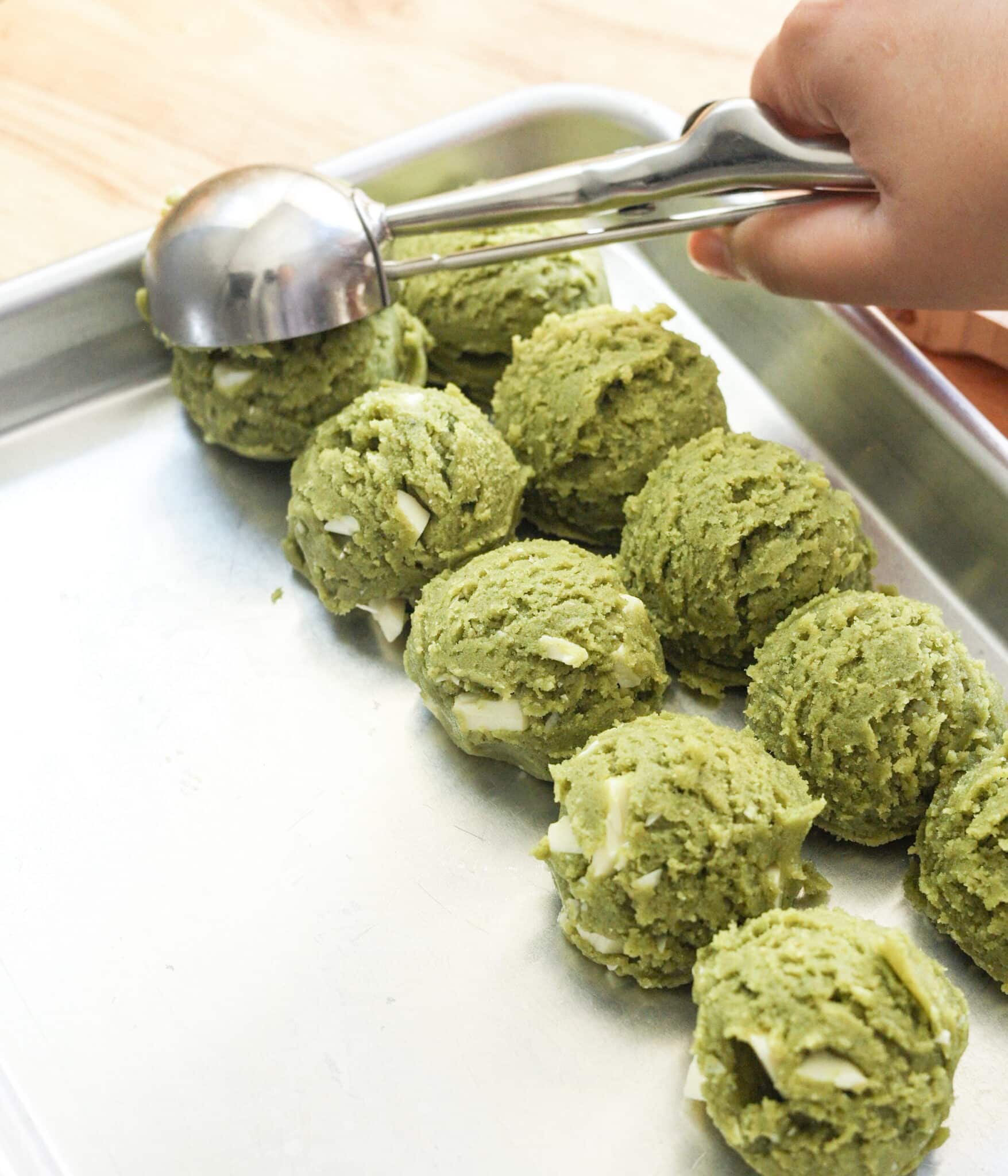 White chocolate matcha cookie dough balls lined up on a baking tray, ready to chill.