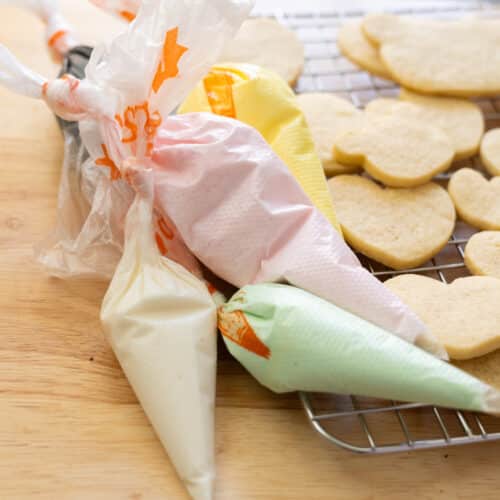 Royal icing in piping bags next to a tray of vanilla bean cut out cookies.