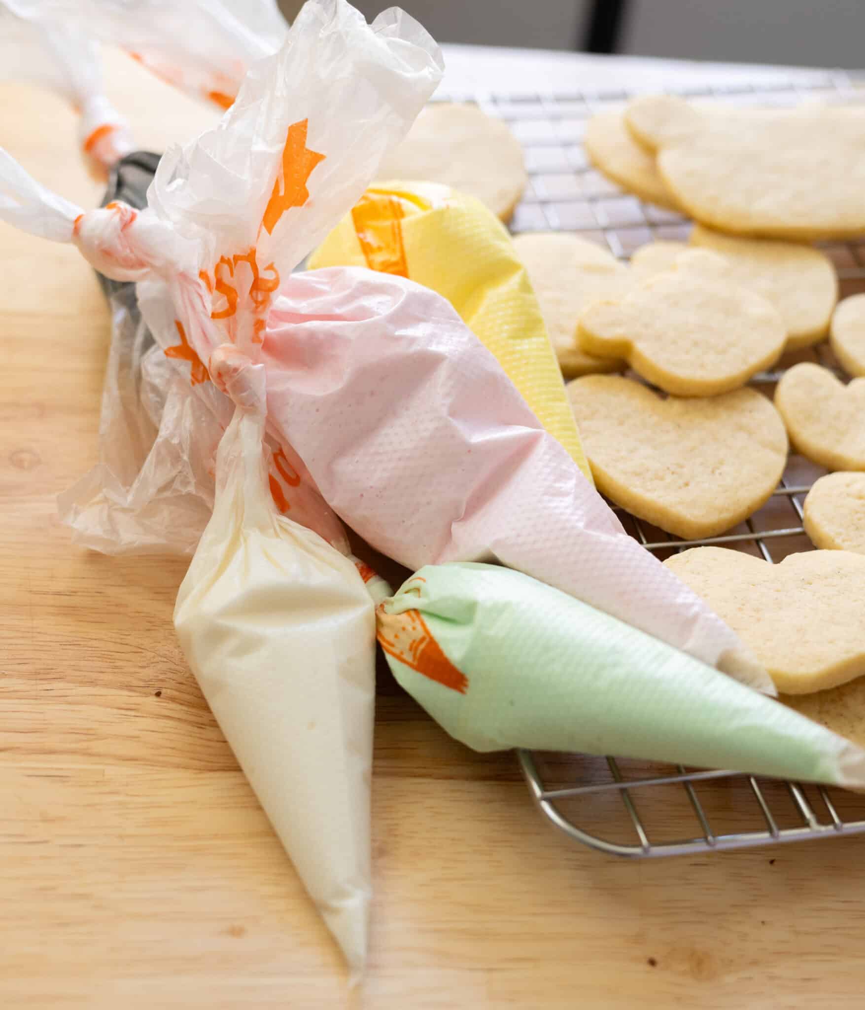 Royal icing in piping bags next to a tray of vanilla bean cut out cookies.