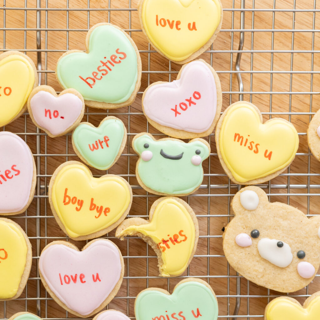 Decorated conversation heart and animal cookies on a wire rack.
