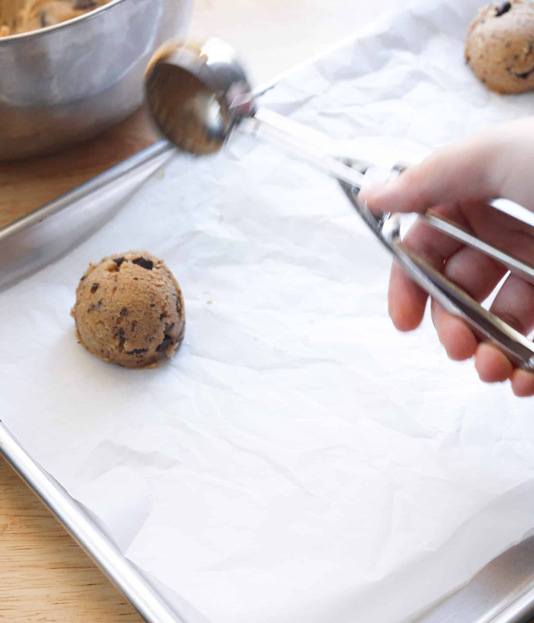 Scooping cookie dough onto lined baking tray.