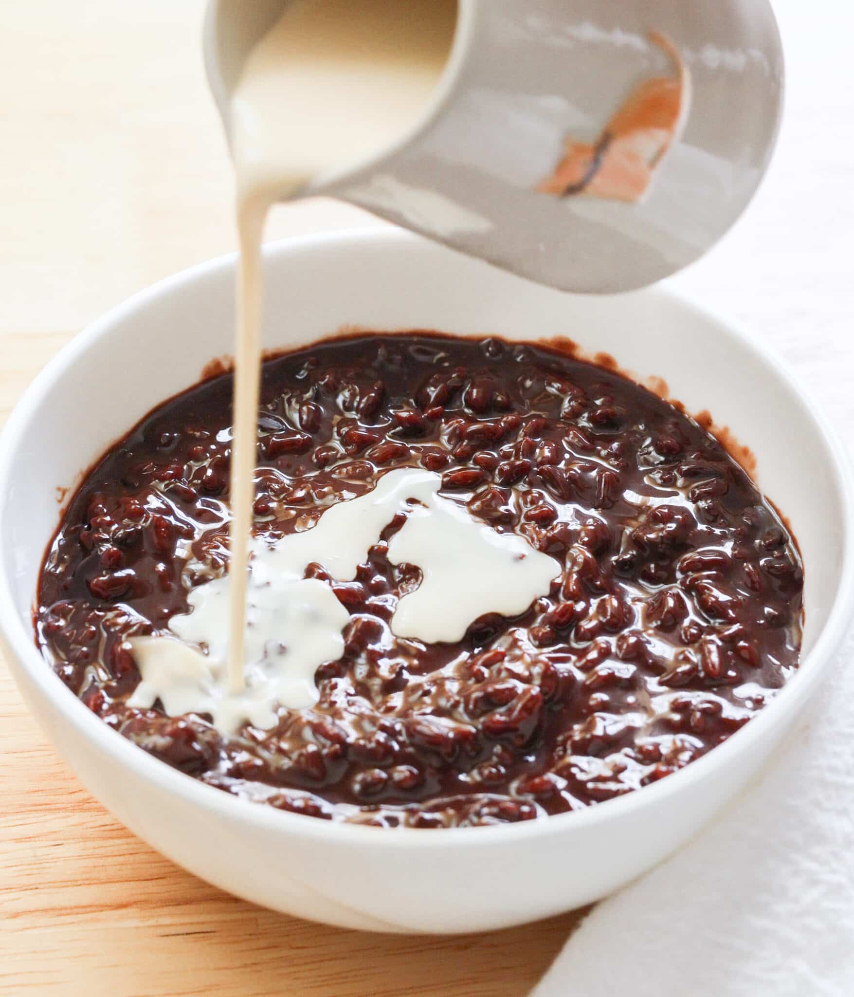 Pouring evaporated milk on top of bowl of chocolate champorado.