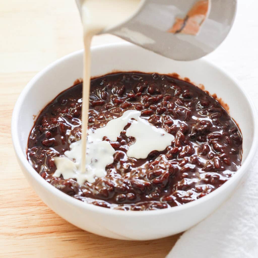Pouring evaporated milk on top of bowl of chocolate champorado.