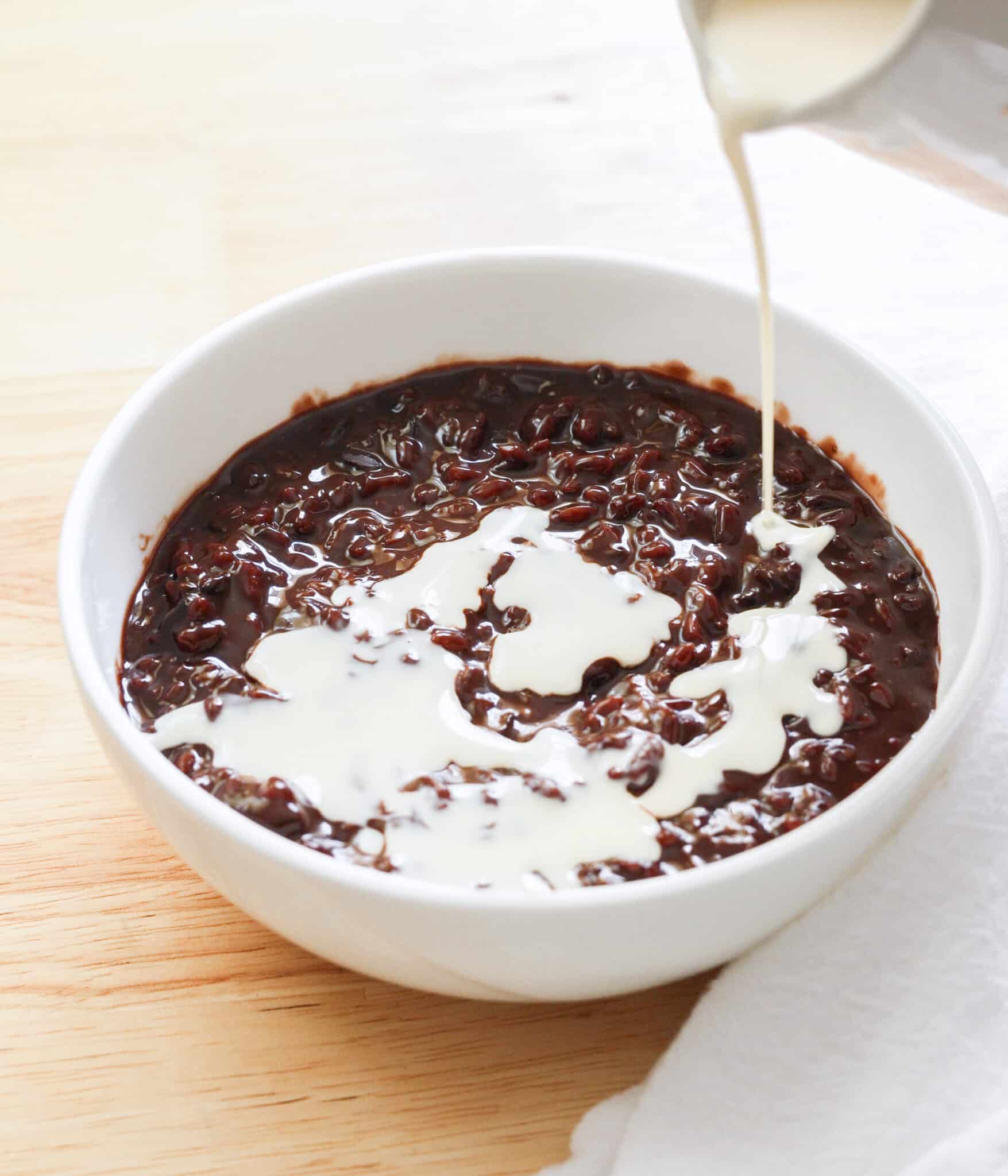 Pouring evaporated milk on top of champorado.