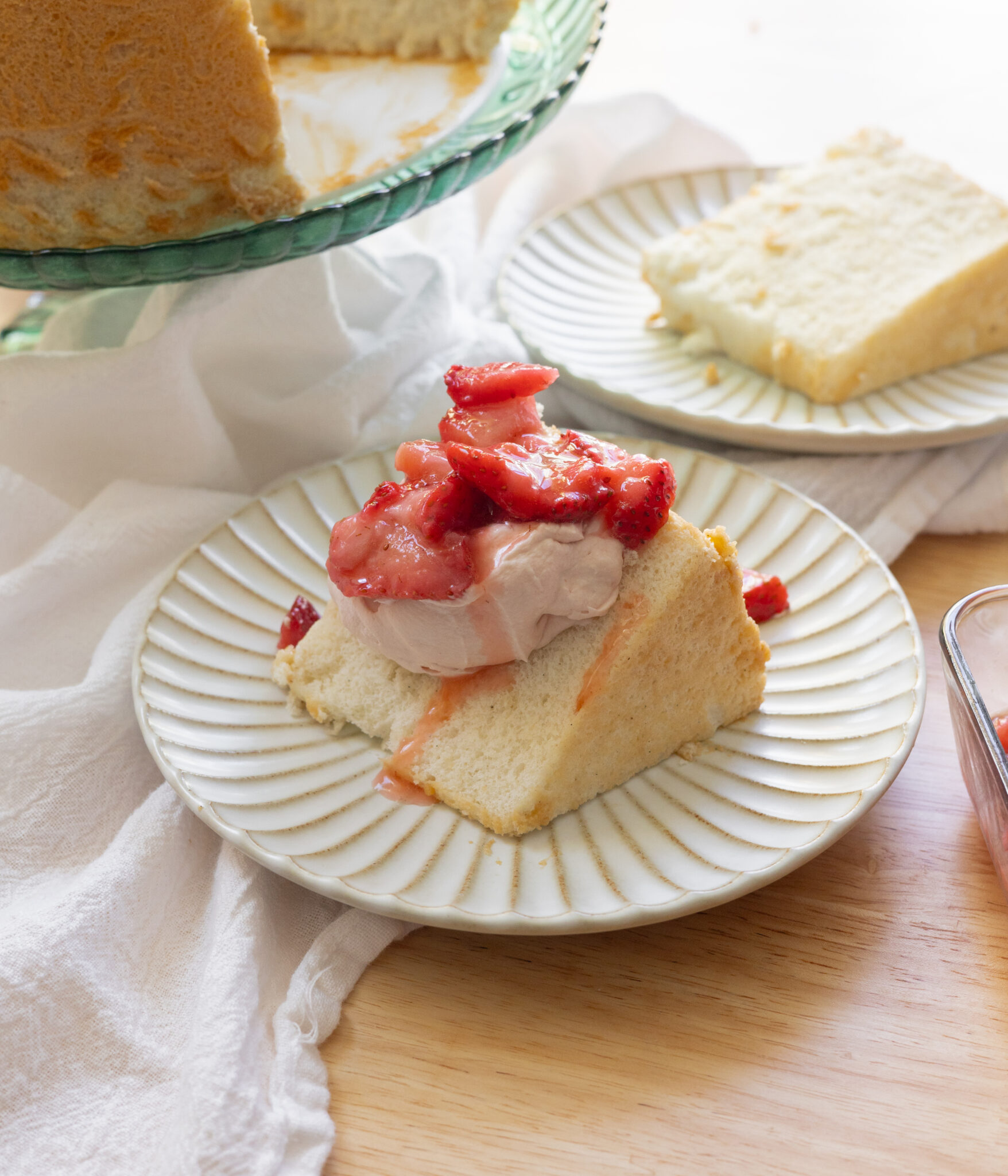 Angel food cake topped with strawberry whipped cream and macerated strawberries.