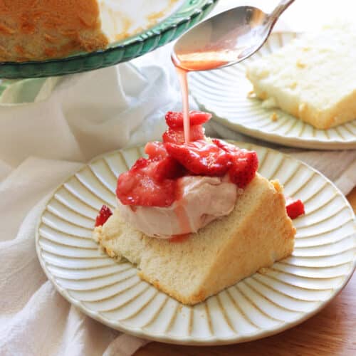 Pouring macerated strawberry juice on top of slice of angel food cake with whipped cream.