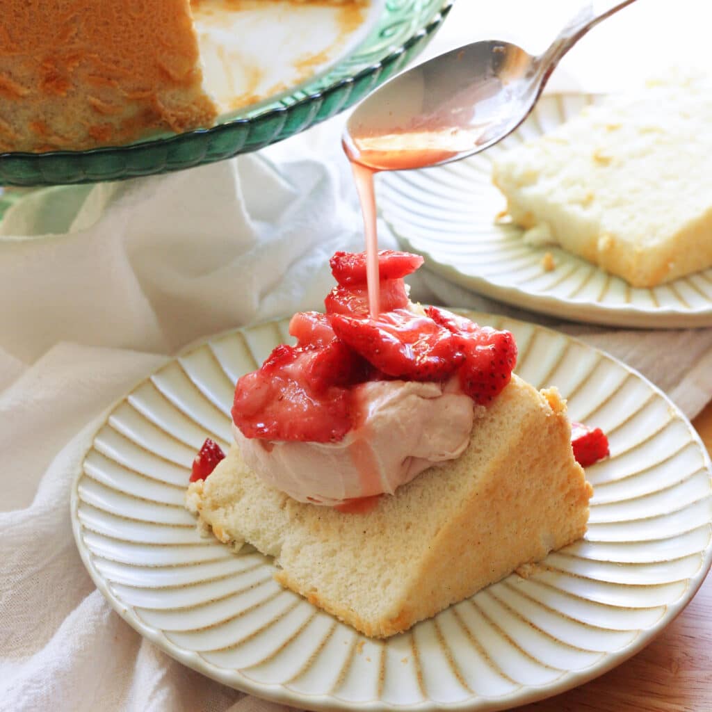 Pouring macerated strawberry juice on top of slice of angel food cake with whipped cream.