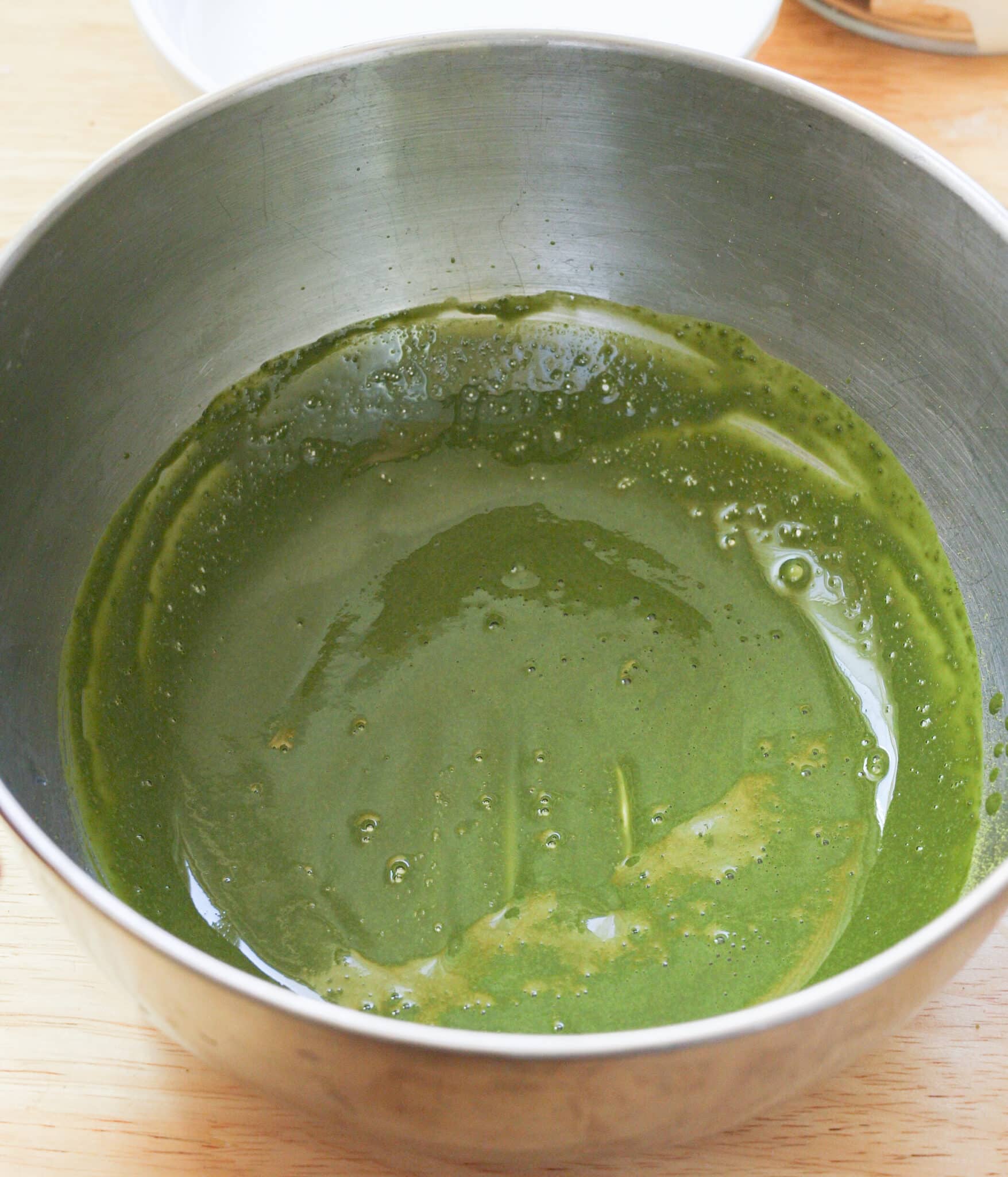 Matcha powder and hot water fully mixed together in a stainless steel bowl.