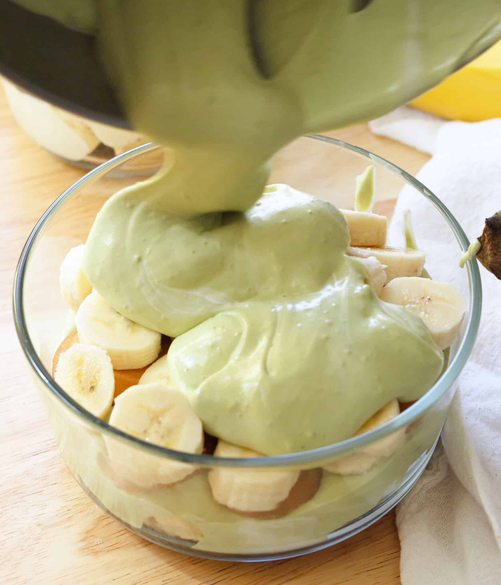 Layering matcha pudding on top of nilla wafers and sliced bananas in a serving bowl.