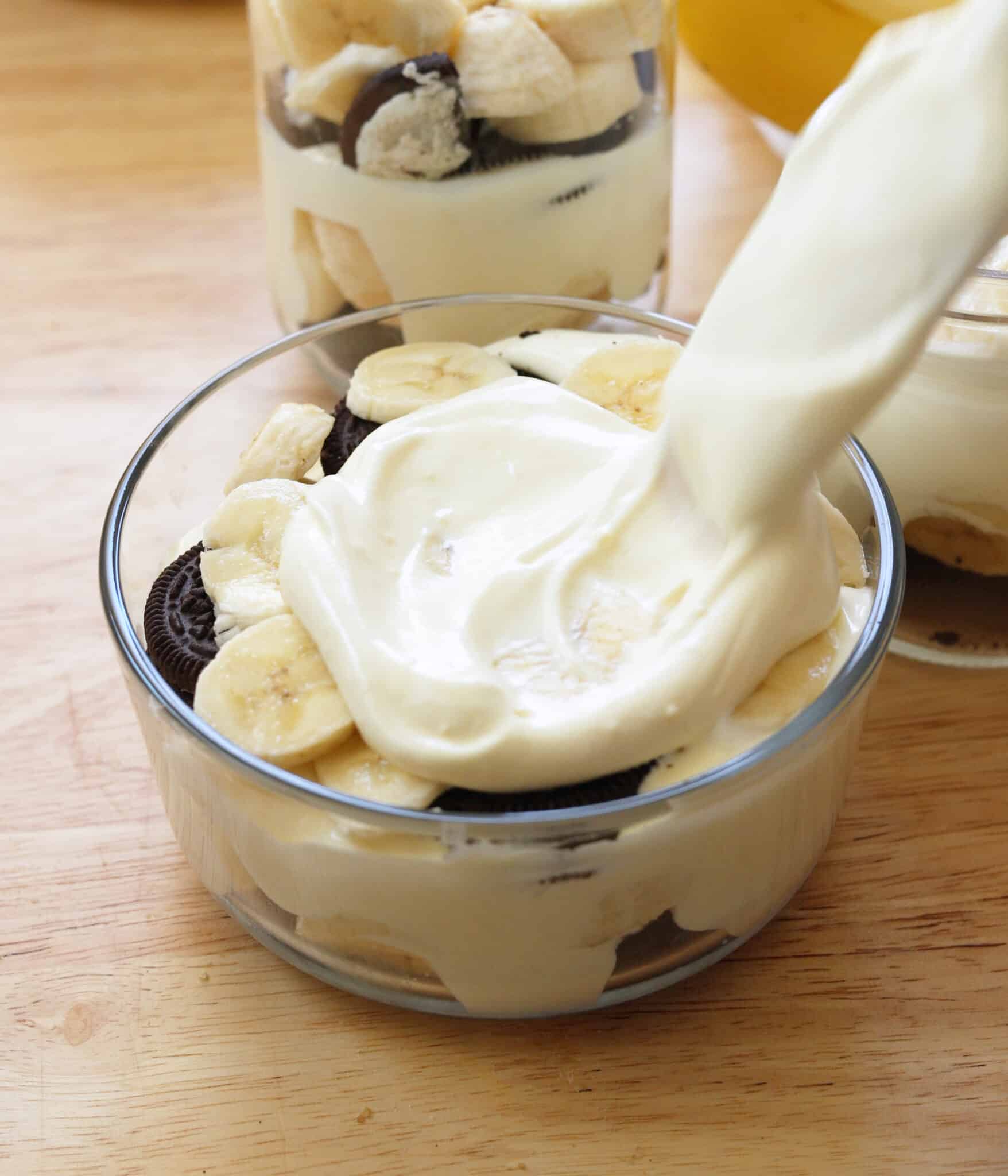 Layering vanilla pudding over Oreos and bananas in a glass container.