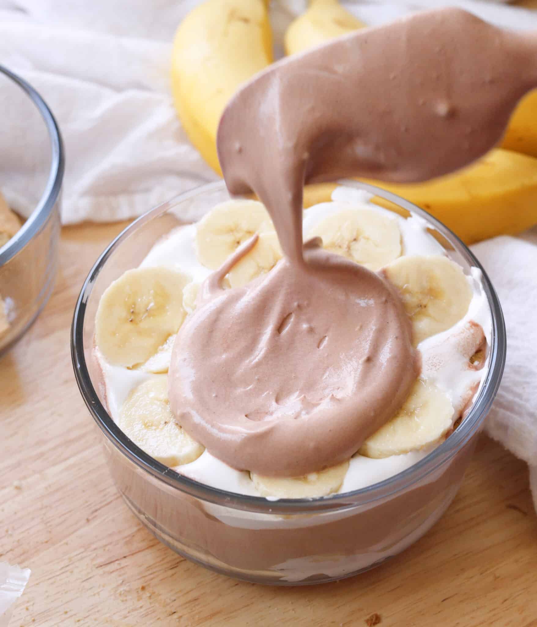 Adding chocolate pudding on top of layers of marshmallow fluff, graham crackers, and bananas.