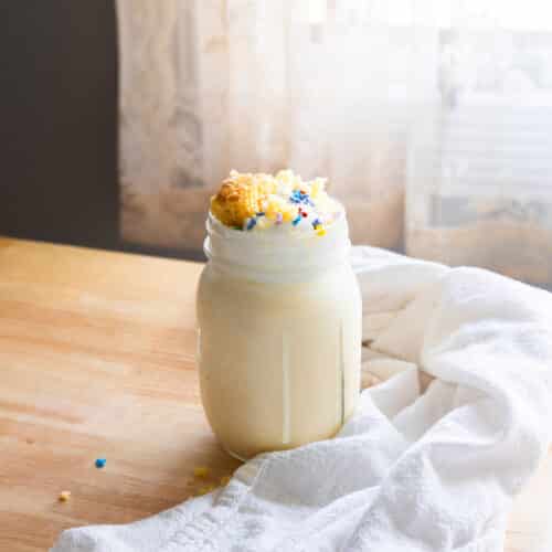 Cake shake in a mason jar topped with whipped cream and rainbow sprinkles.