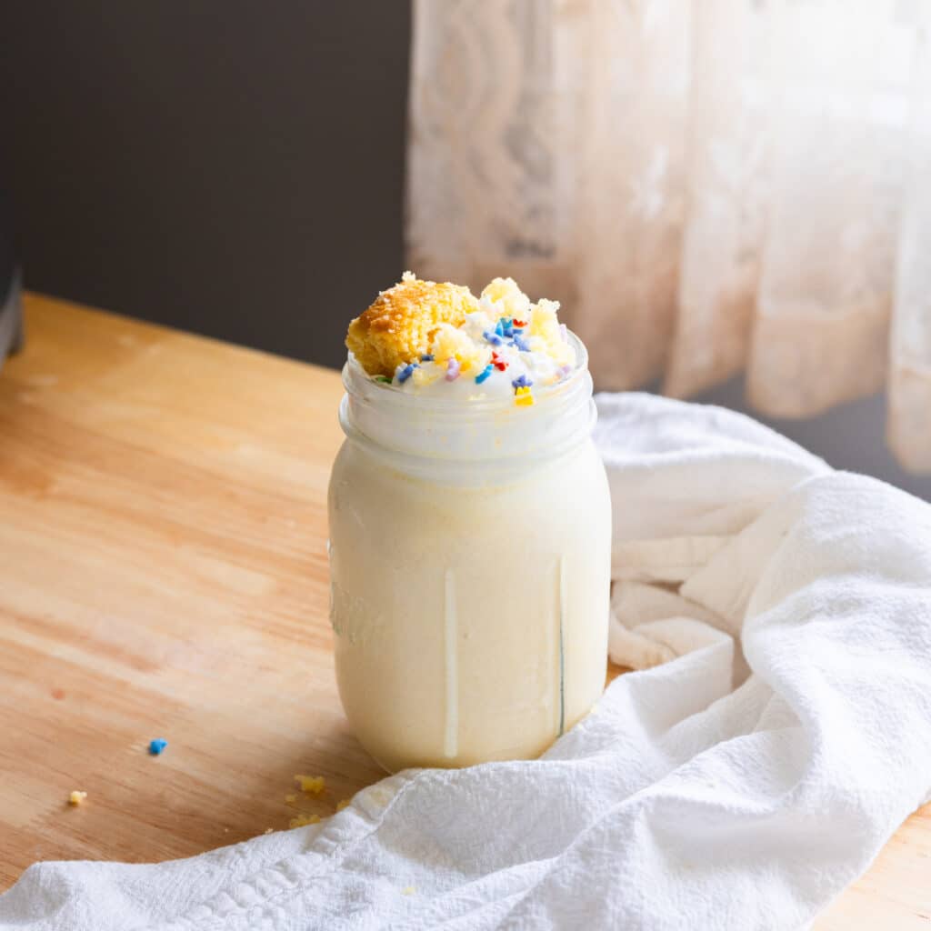 Cake shake in a mason jar topped with whipped cream and rainbow sprinkles.