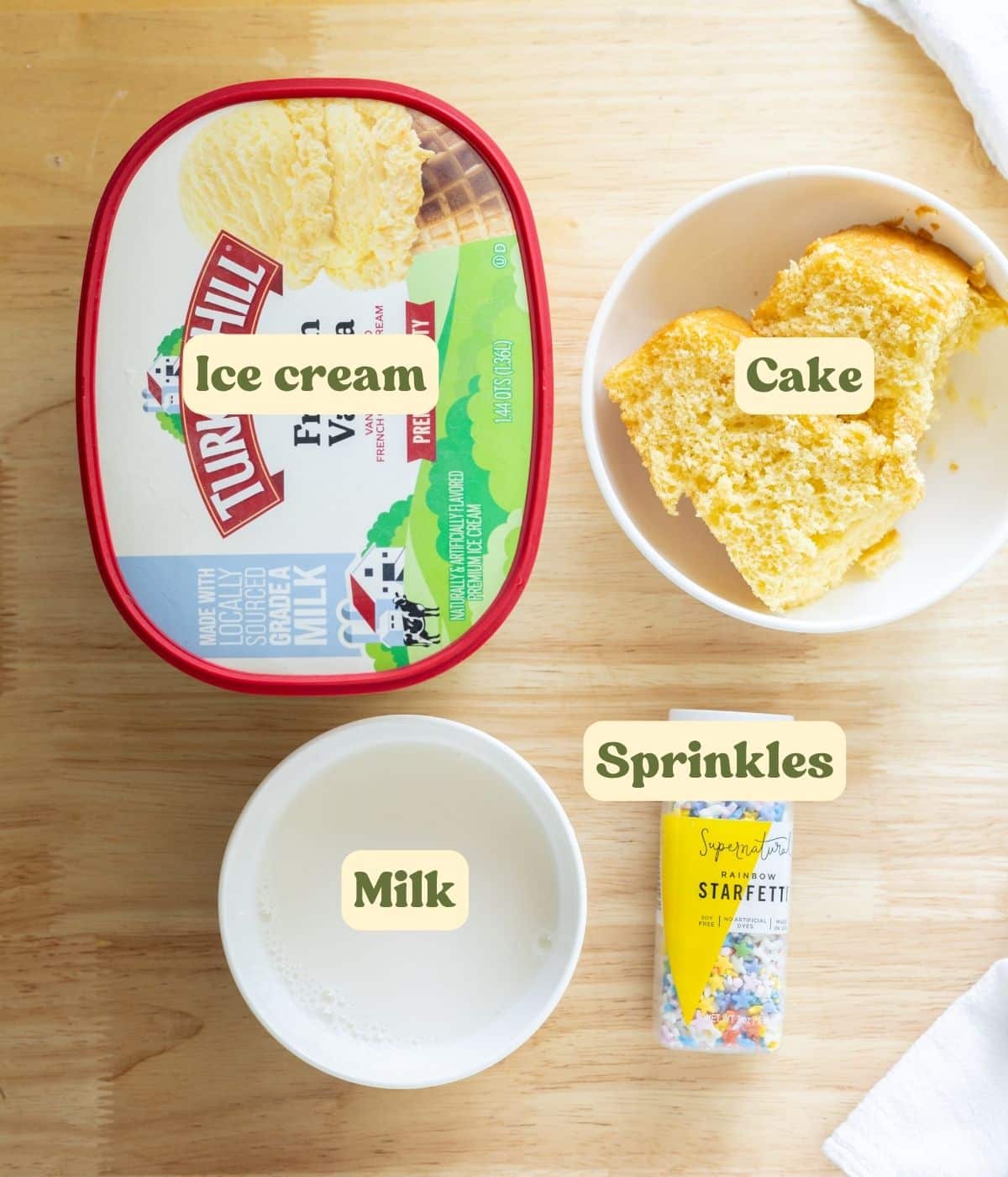 Birthday cake shake labeled ingredients laid out on a wooden table.