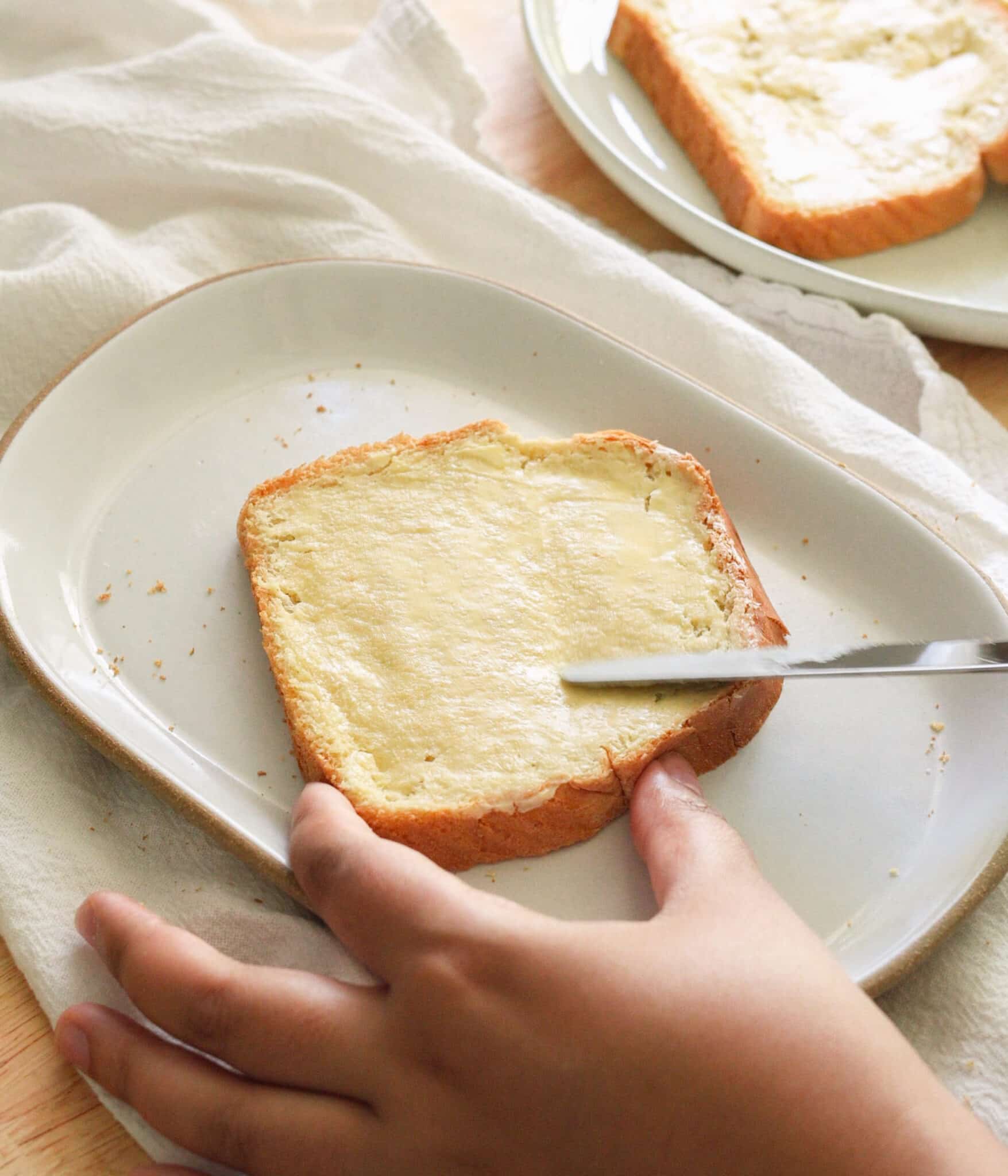 Spreading salted butter on soft white bread with a knife.
