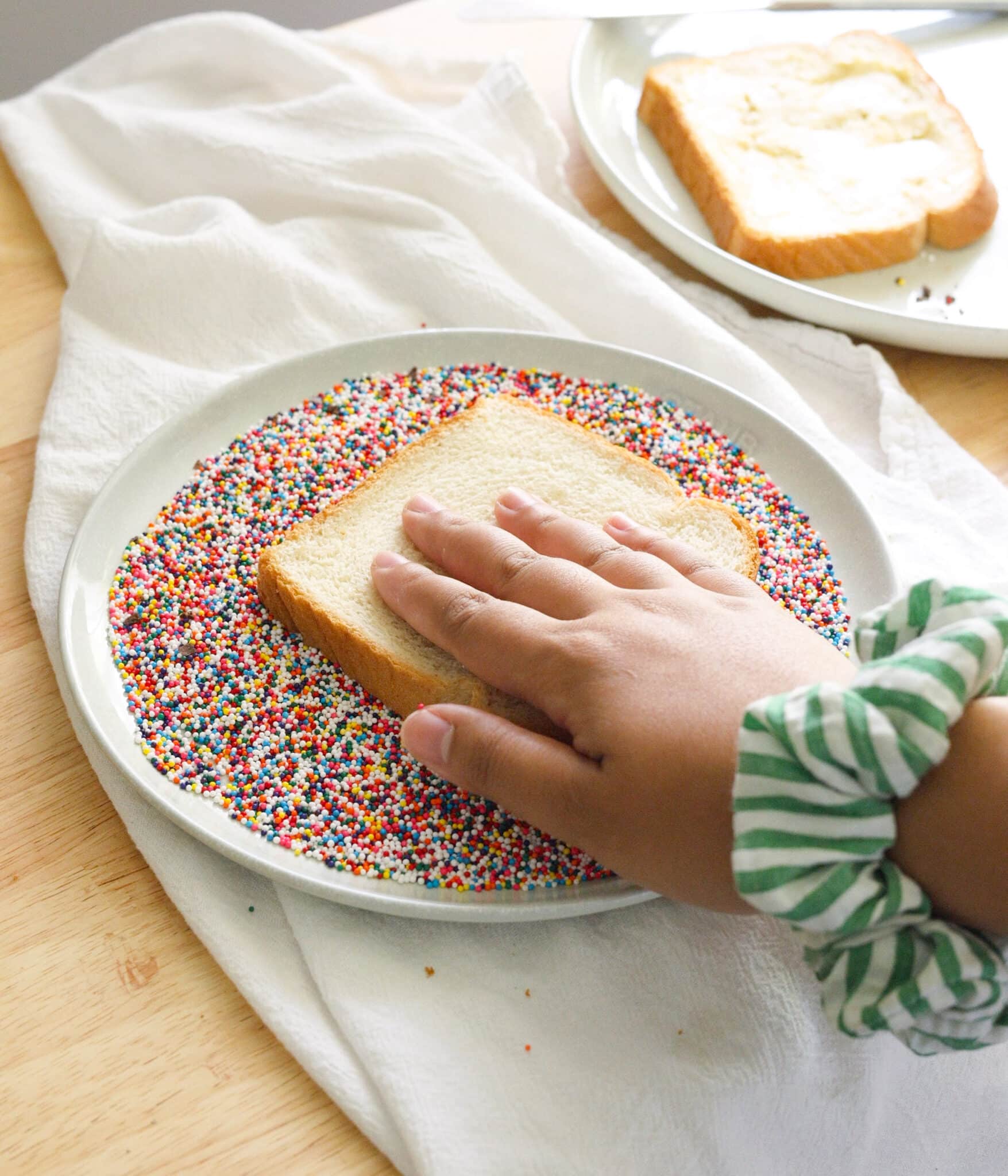 Dipping buttered white bread into hundreds and thousands.