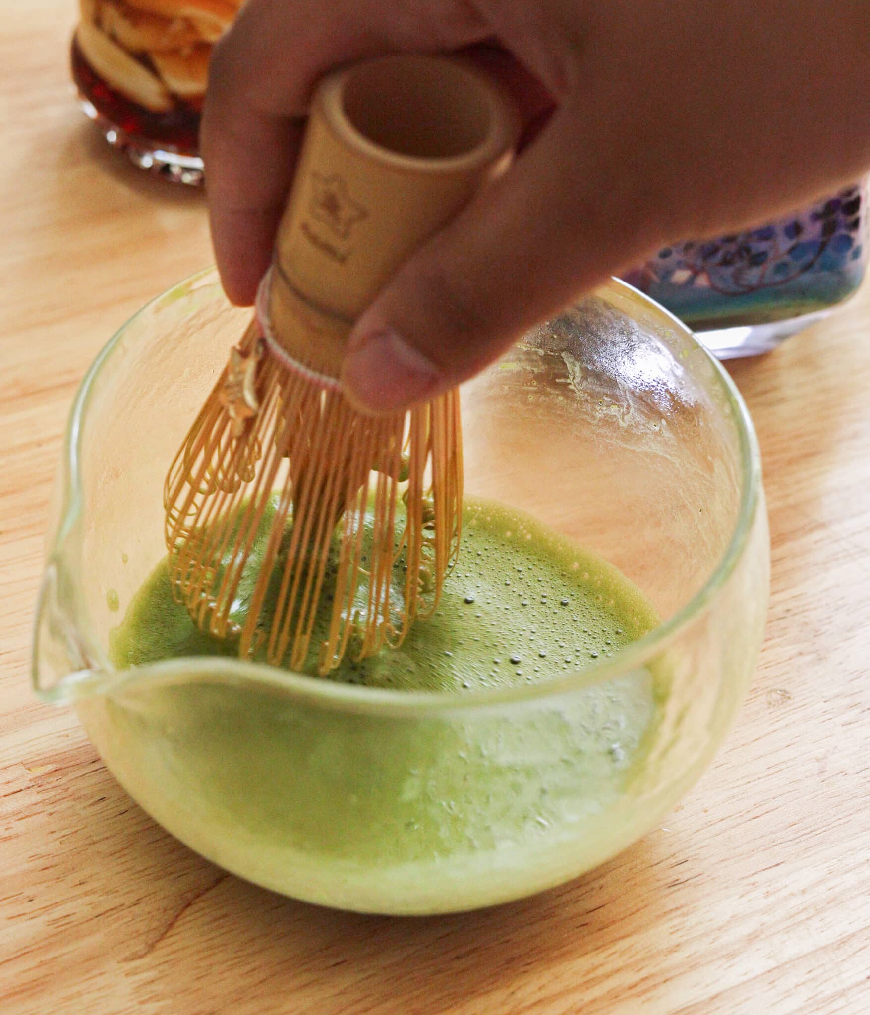 Whisking matcha powder and hot water in a glass bowl.