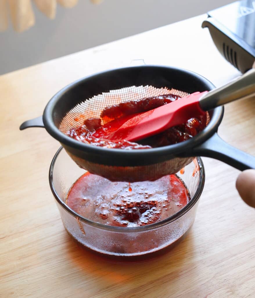 Straining strawberry syrup into a glass container.