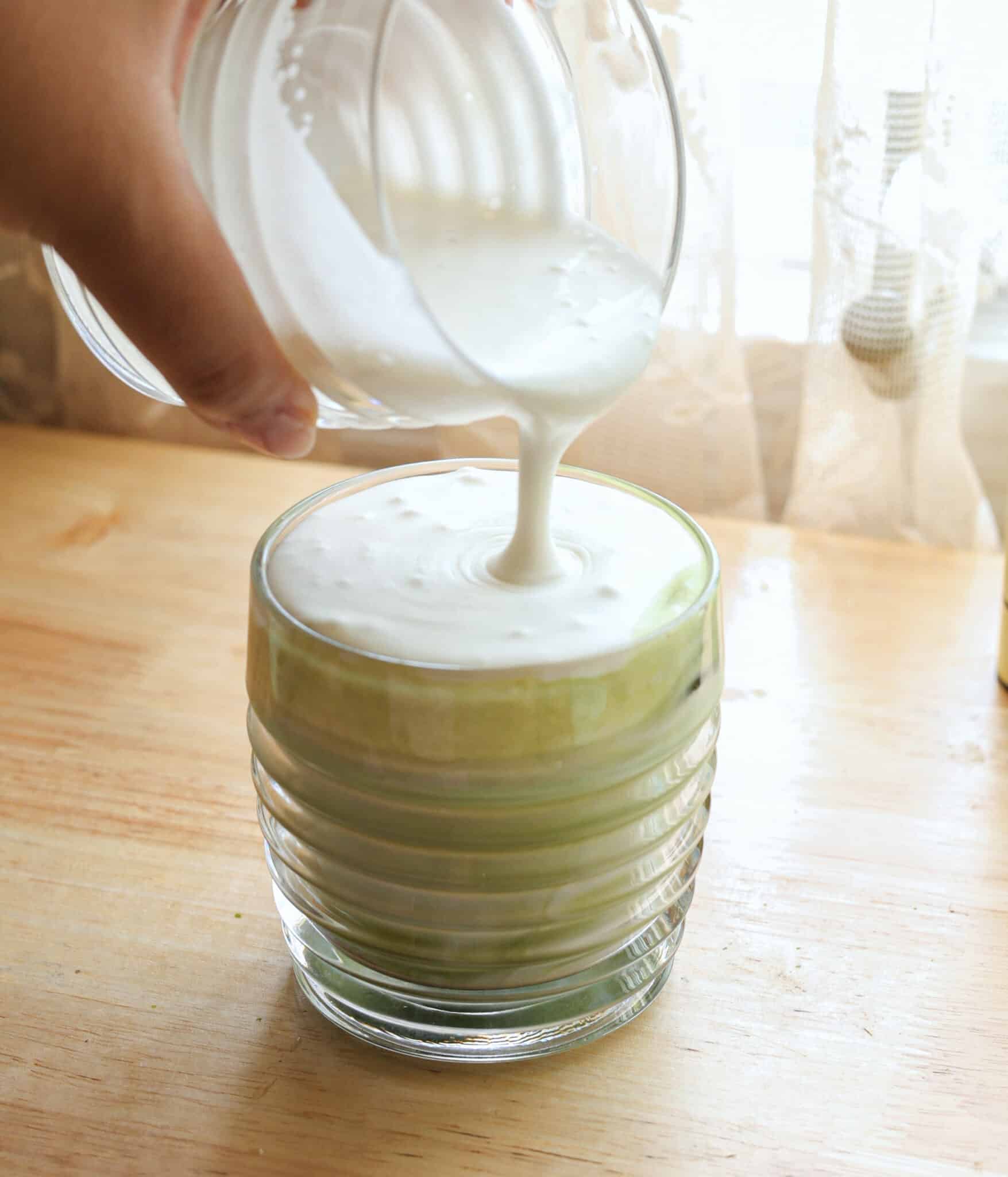 Pouring coconut cold foam on top of a matcha latte.