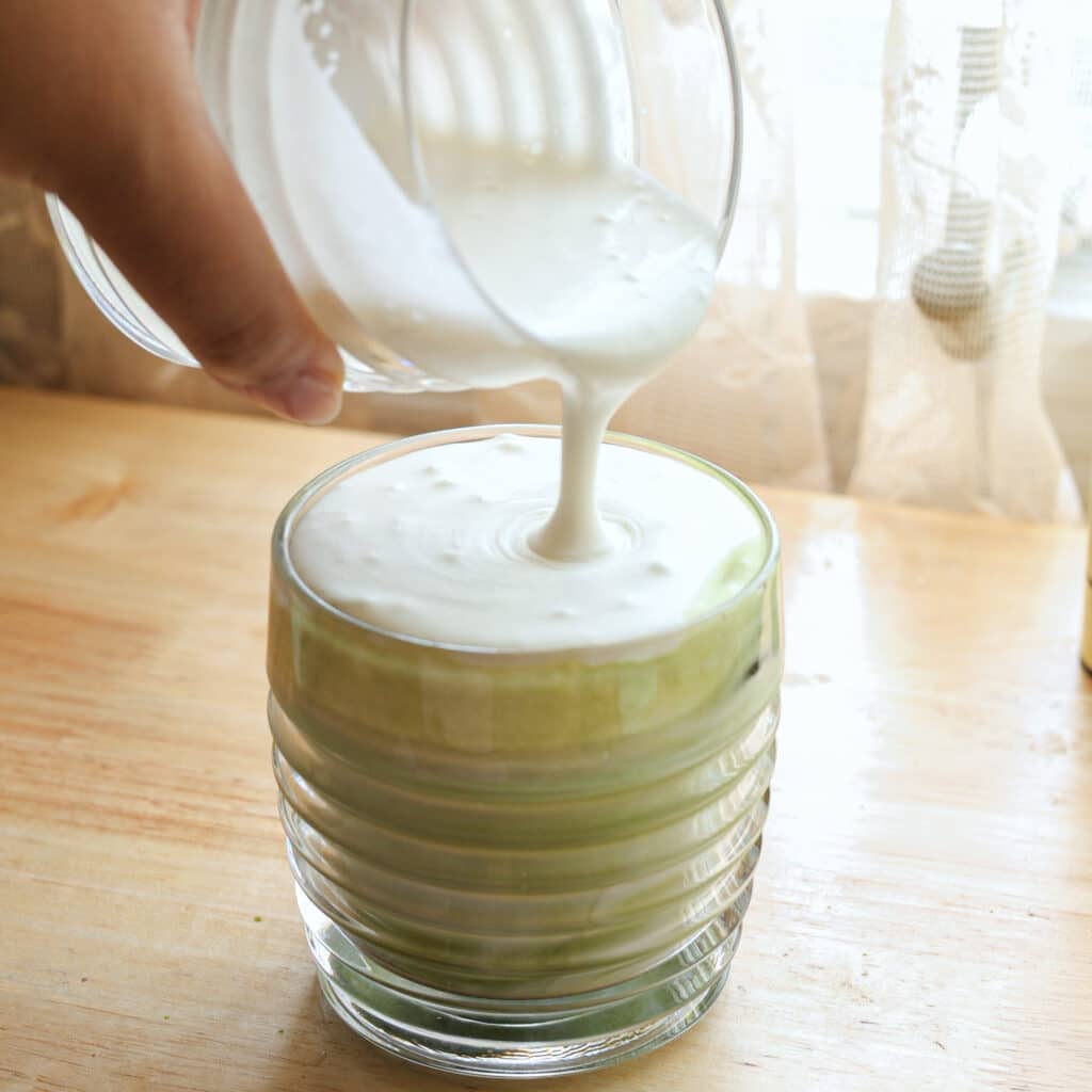 Pouring coconut cold foam on top of a matcha latte.