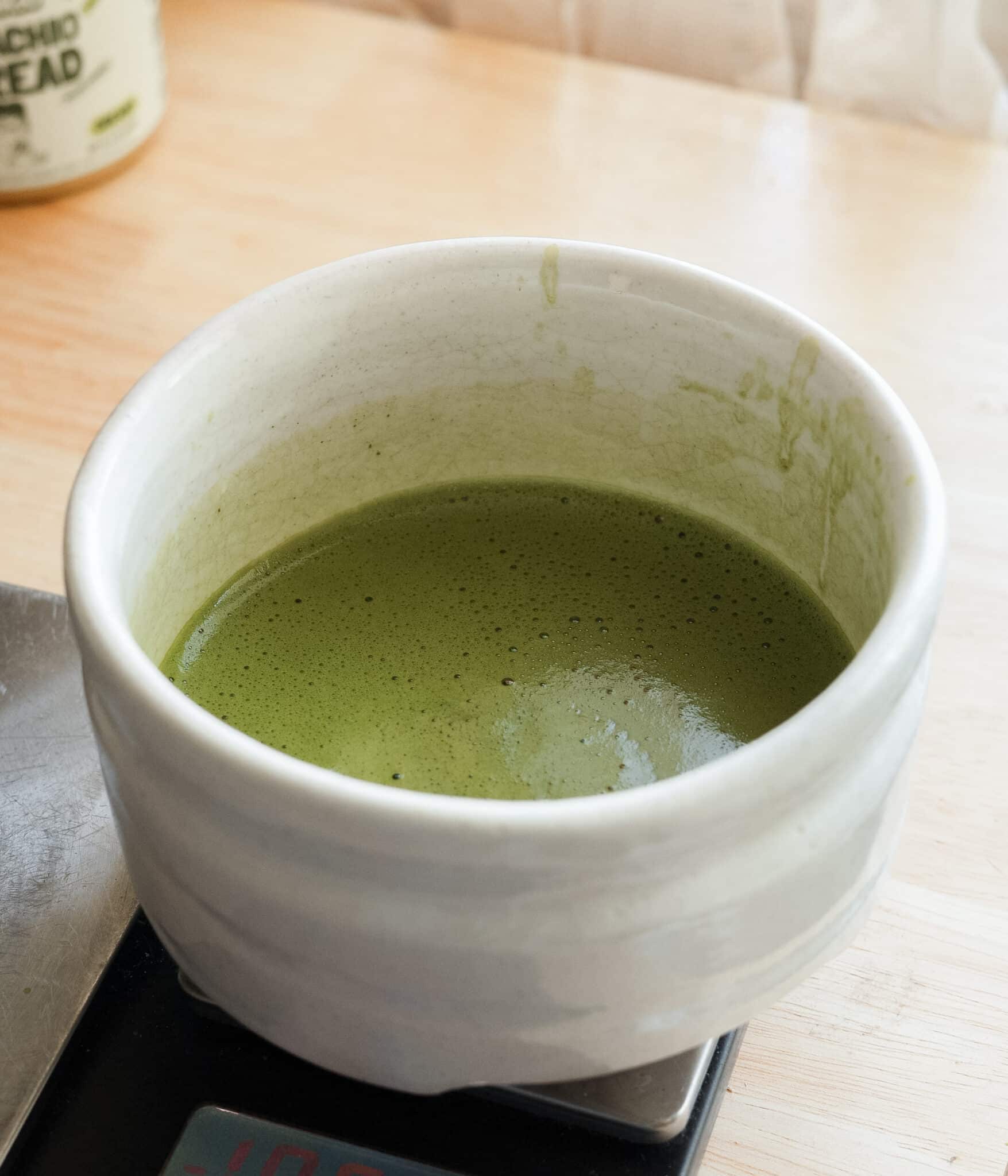 Brewed matcha tea in a white bowl.