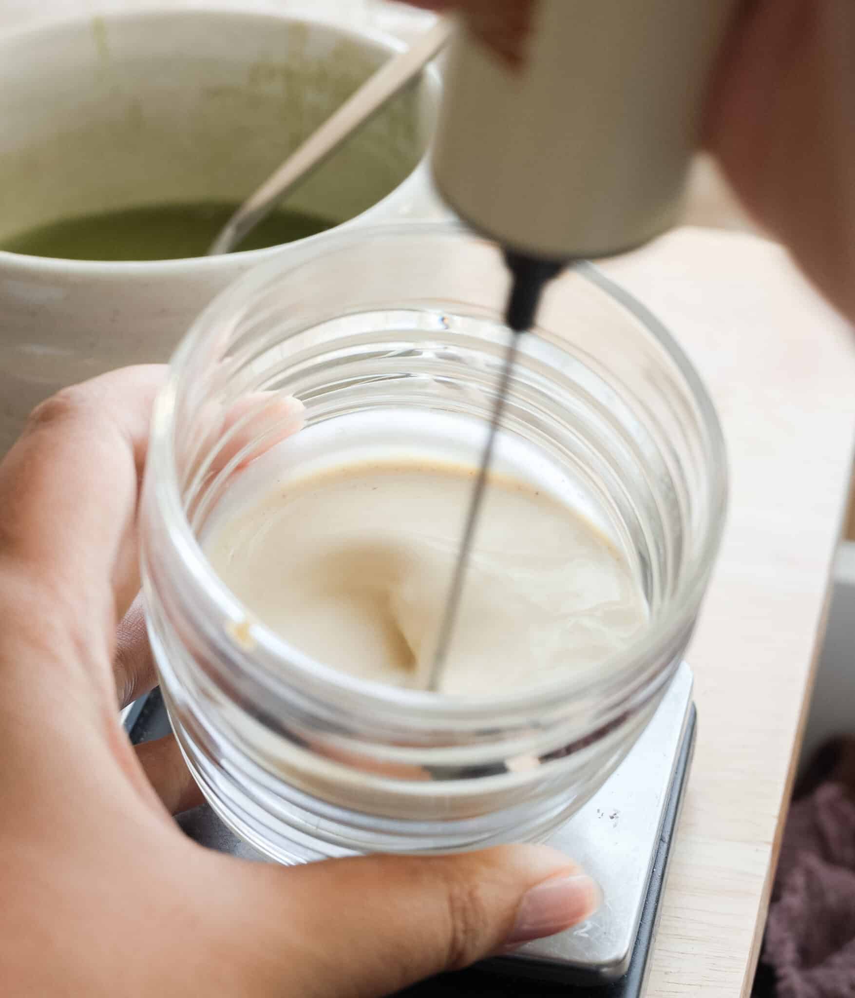 Pouring matcha mixture into a cup of oat milk.