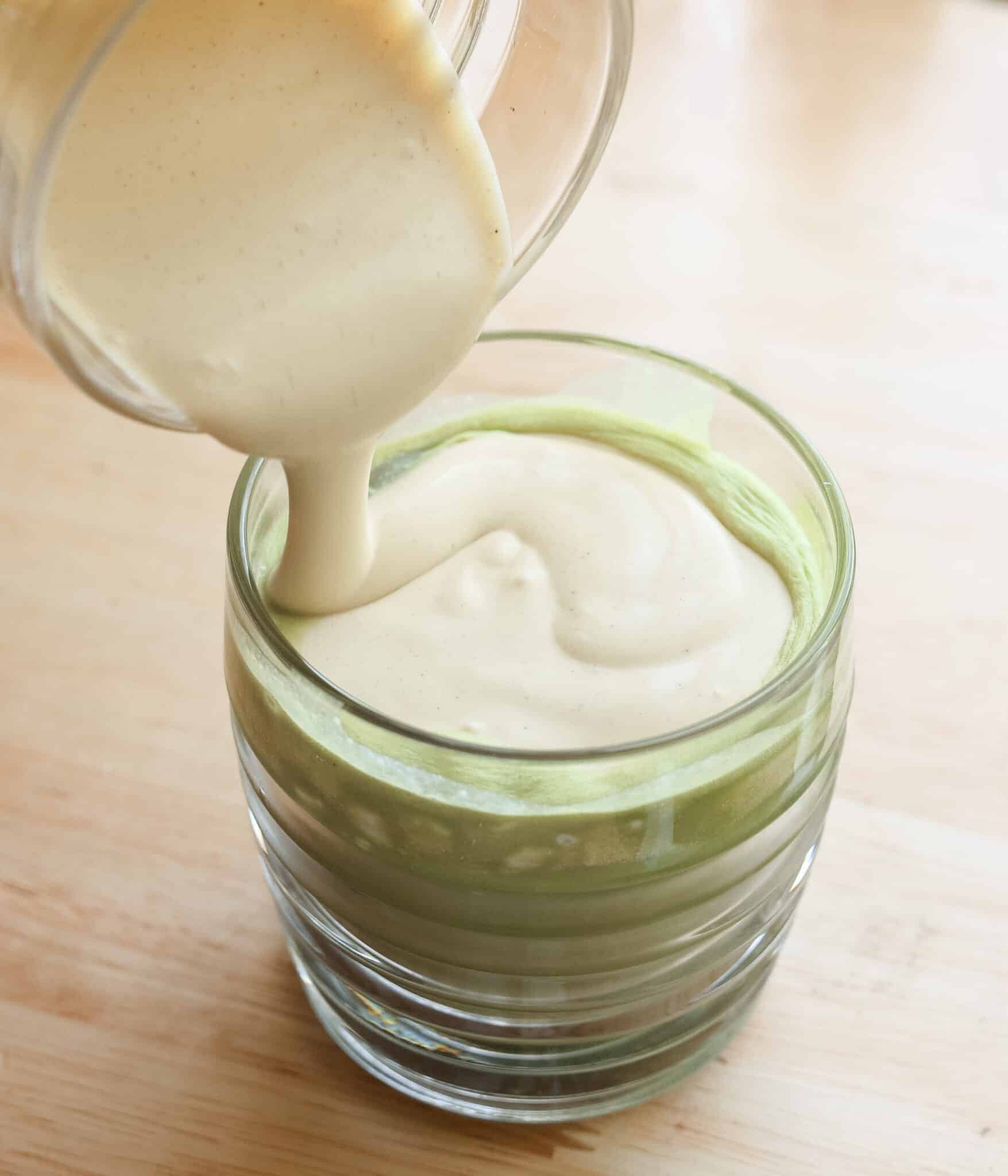 Pouring creamy pistachio cold foam over matcha latte.