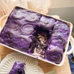 Ube cinnamon rolls topped with ube cream cheese frosting in a ceramic dish.