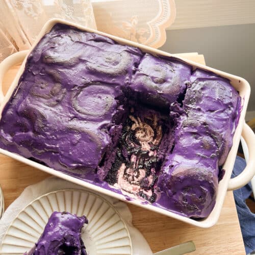 Ube cinnamon rolls topped with ube cream cheese frosting in a ceramic dish.