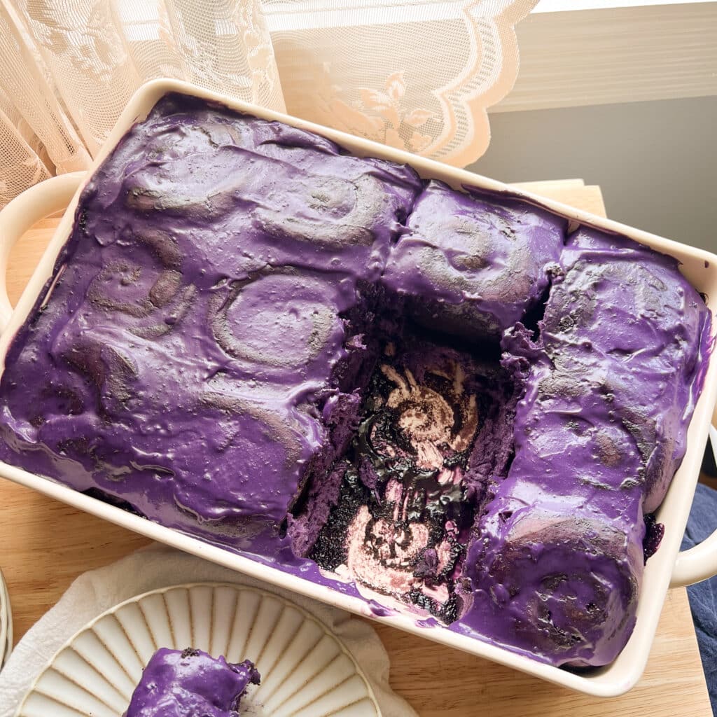 Ube cinnamon rolls topped with ube cream cheese frosting in a ceramic dish.