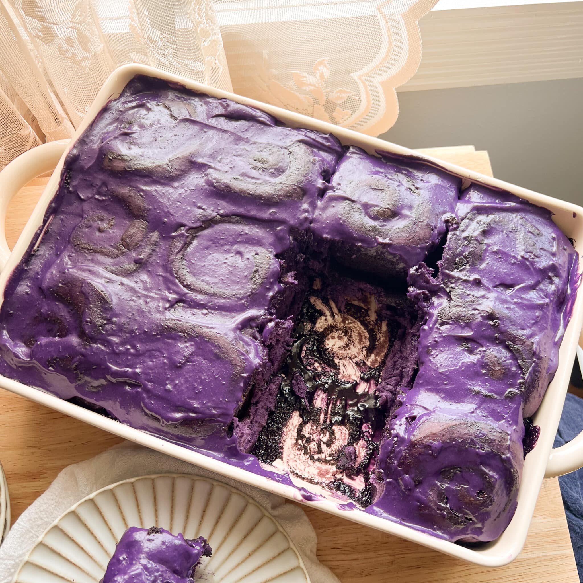 Ube cinnamon rolls topped with ube cream cheese frosting in a ceramic dish.