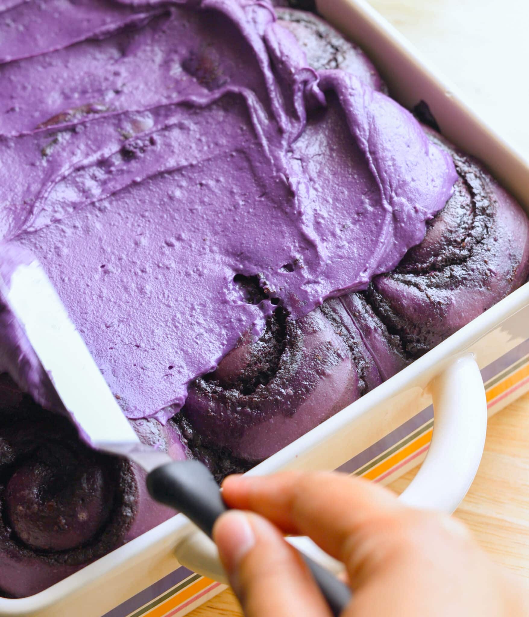 Spreading ube frosting on top of ube brioche cinnamon rolls.